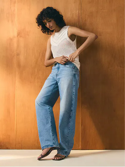 Woman wearing light blue curved-leg barrel jeans with a sleeveless white top.