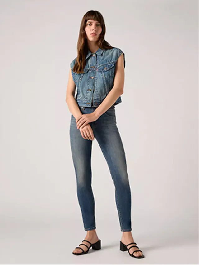 Woman dressed in skinny jeans and sleeveless denim top with casual stance.