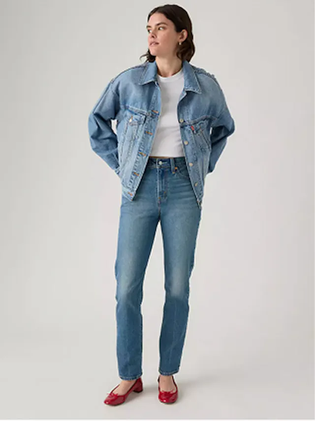 Woman wearing slim-fit jeans and denim jacket with hands in pockets.