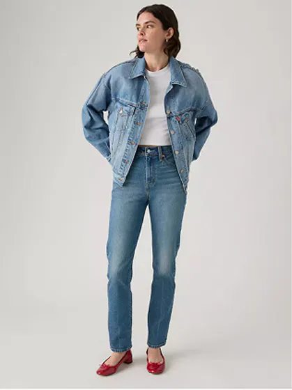 Woman wearing slim-fit jeans and denim jacket with hands in pockets.