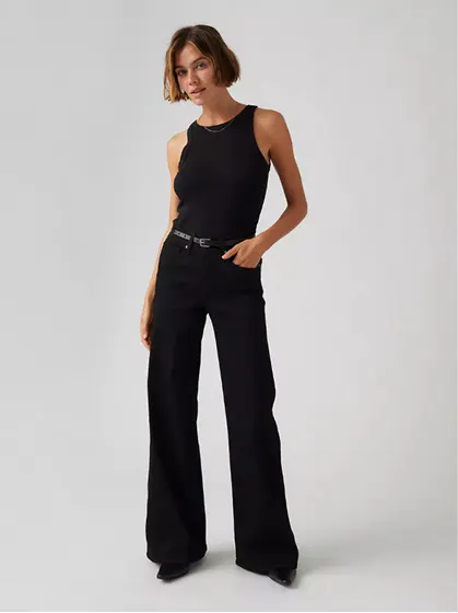 Woman in black wide-leg jeans and sleeveless top posing confidently.