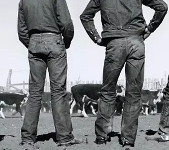 A black and white image of two men stood facing away from the camera. Focus on jeans.