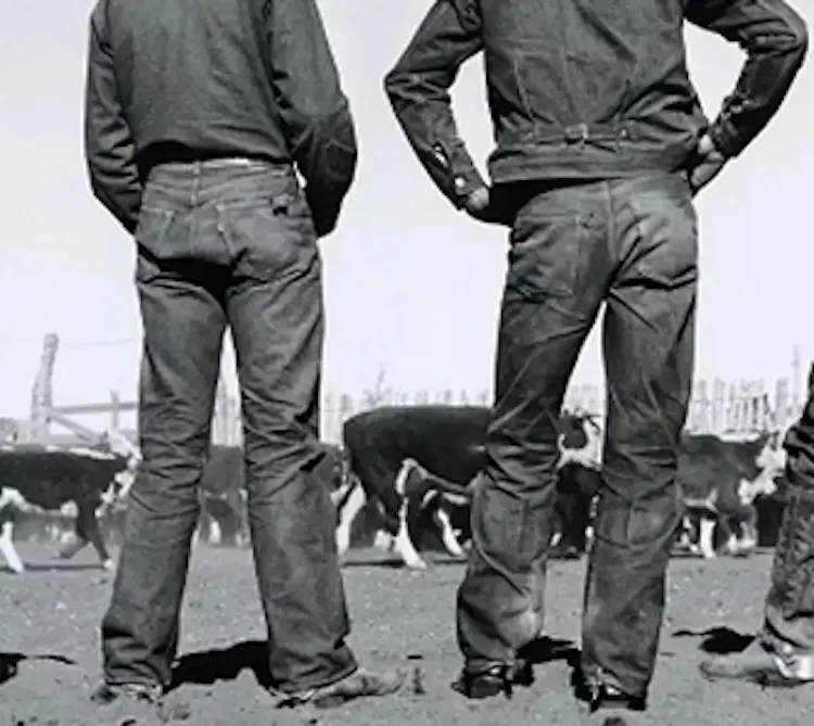 A black and white image of two men stood facing away from the camera. Focus on jeans.