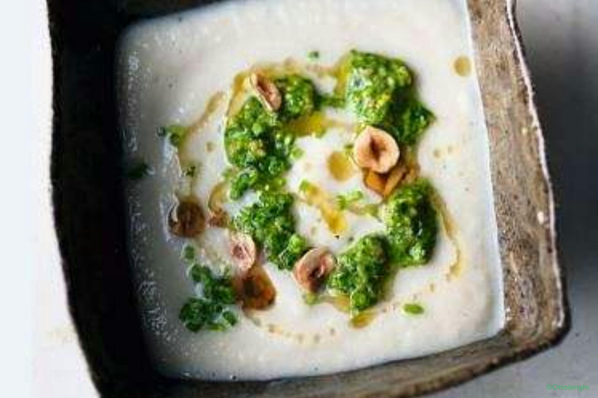 een vierkante kom met witte aardpeer soep met spinaziepesto