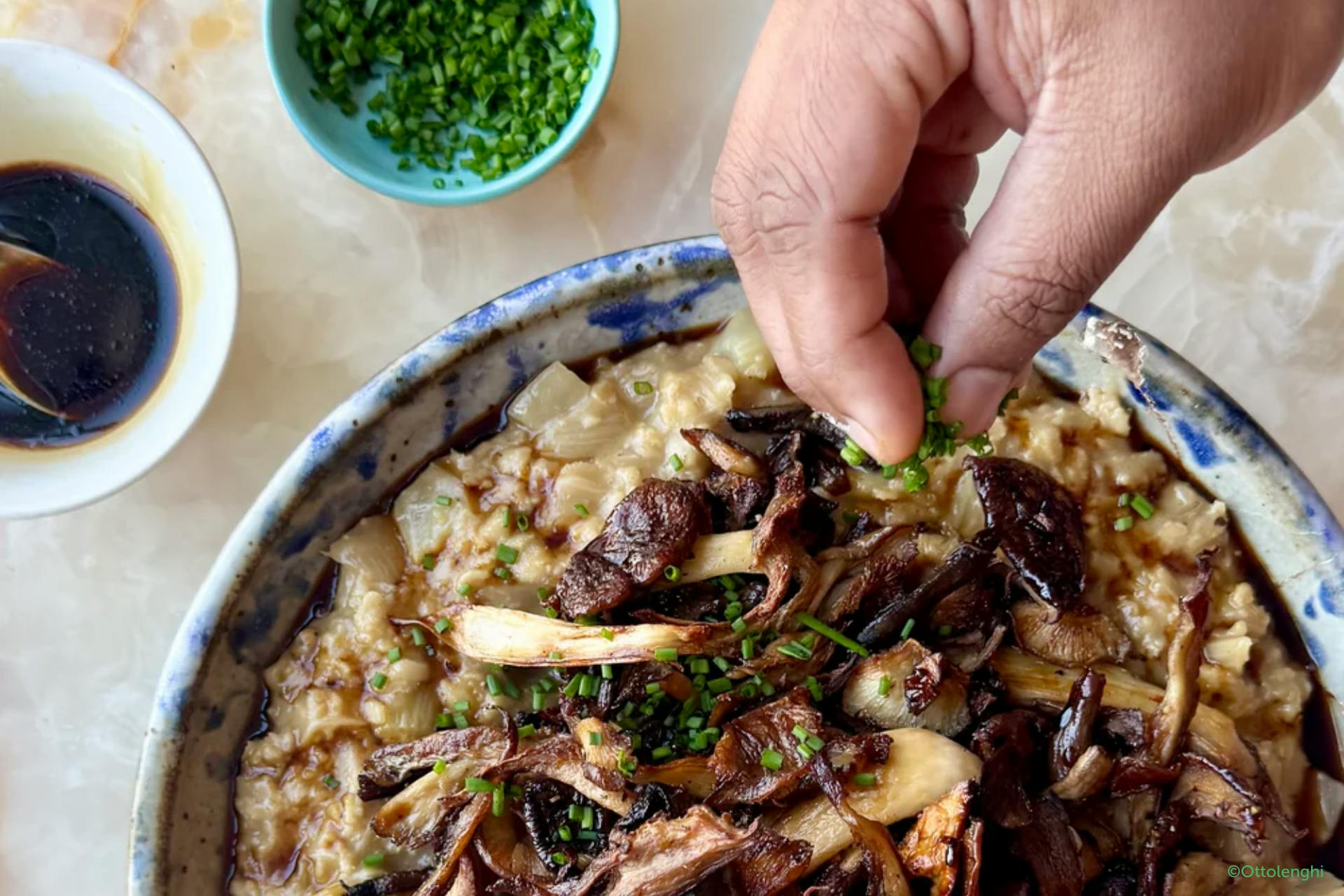 Foto van hand die kruiden toevoegt aan schotel met vegan risotto met oesterzwammen