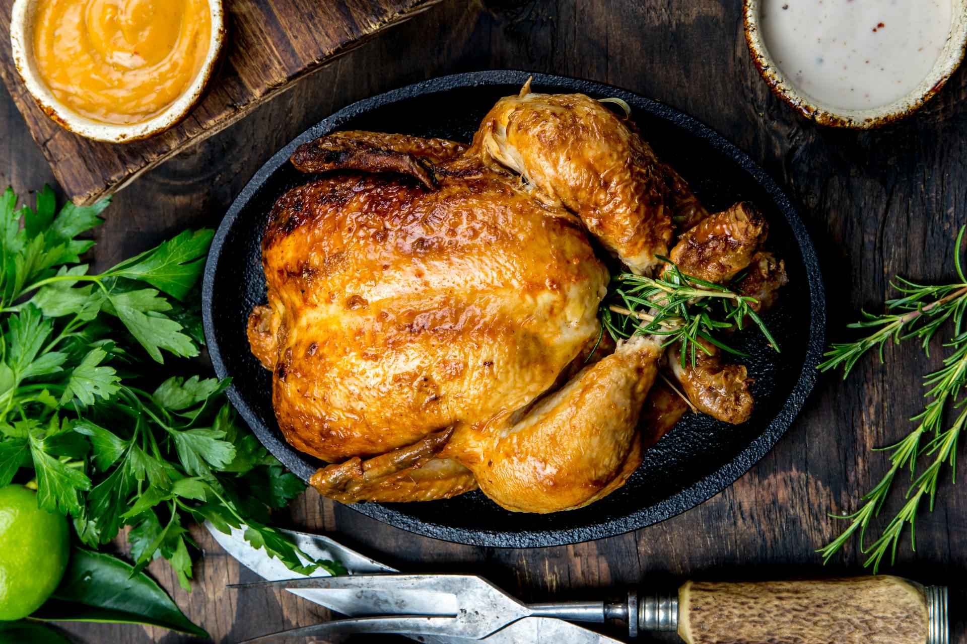 Fot van braadkip in braadpan op houten tafel omringt met kruiden, saus en bestek