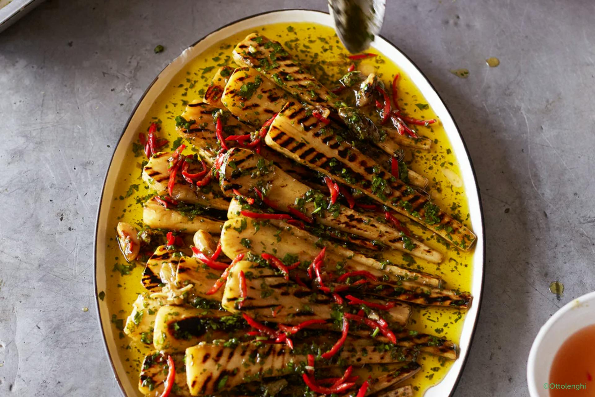 Foto met een ovalen schaal gevuld met gegrilde pastinaak in olie en kruiden


