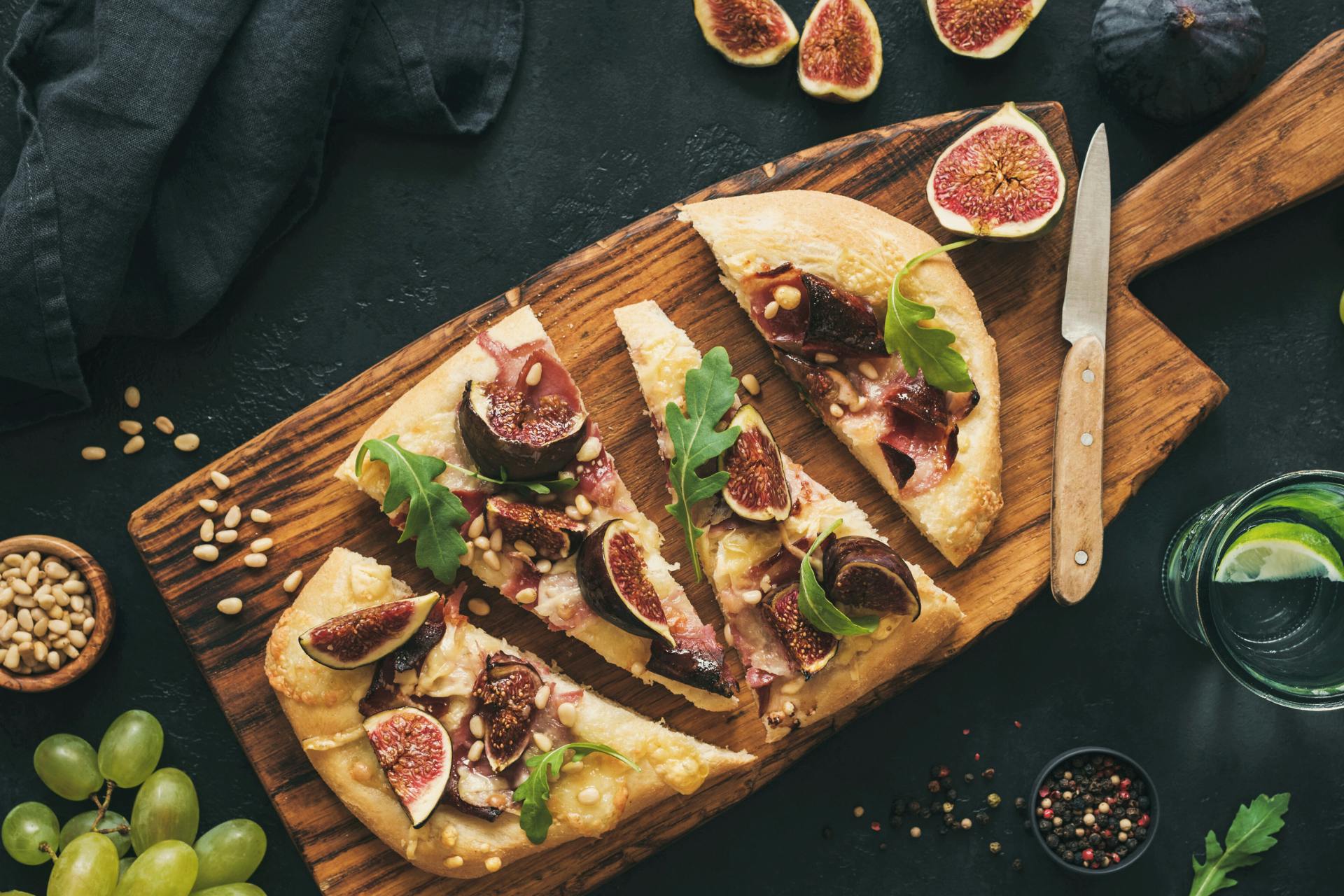 Foto van pizza met vijgen op plank en pijnboompitten