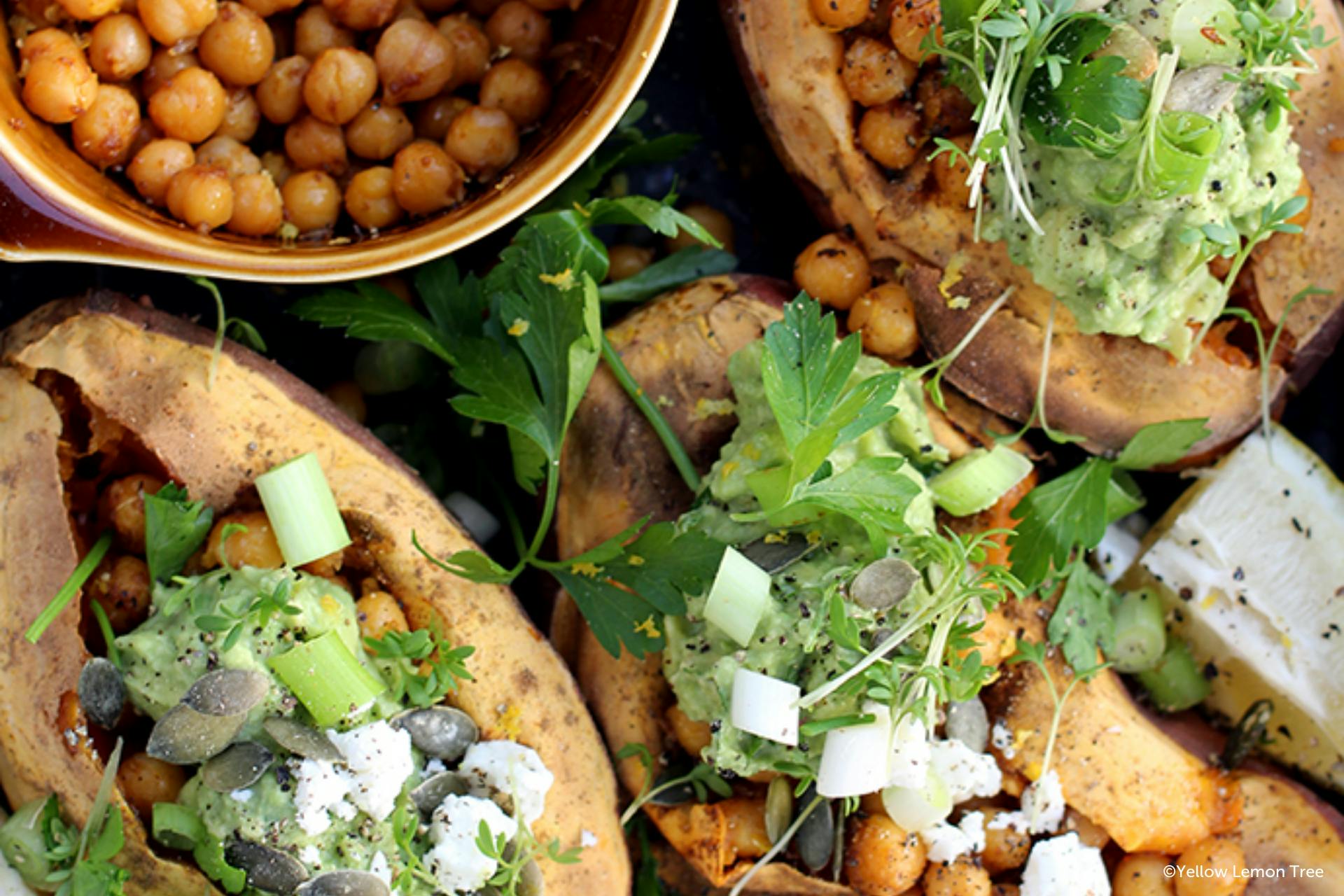 Foto van een gepofte bataat met kikkererwten, feta, pompoenpitten en avocado-tahinsaus