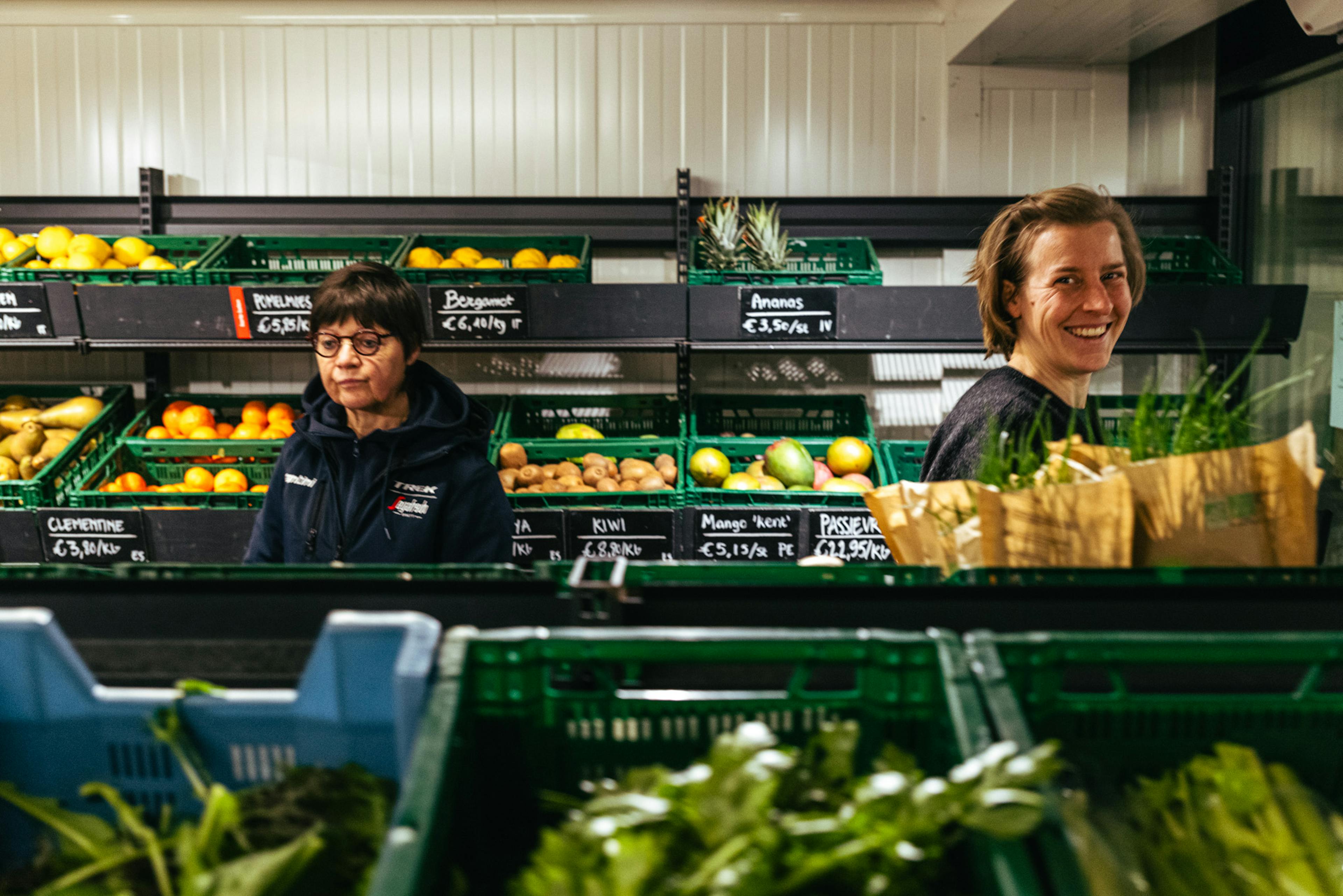 Klanten in de koelafdeling van de winkel op de boerderij tussen de bakken met versgeoogste groenten