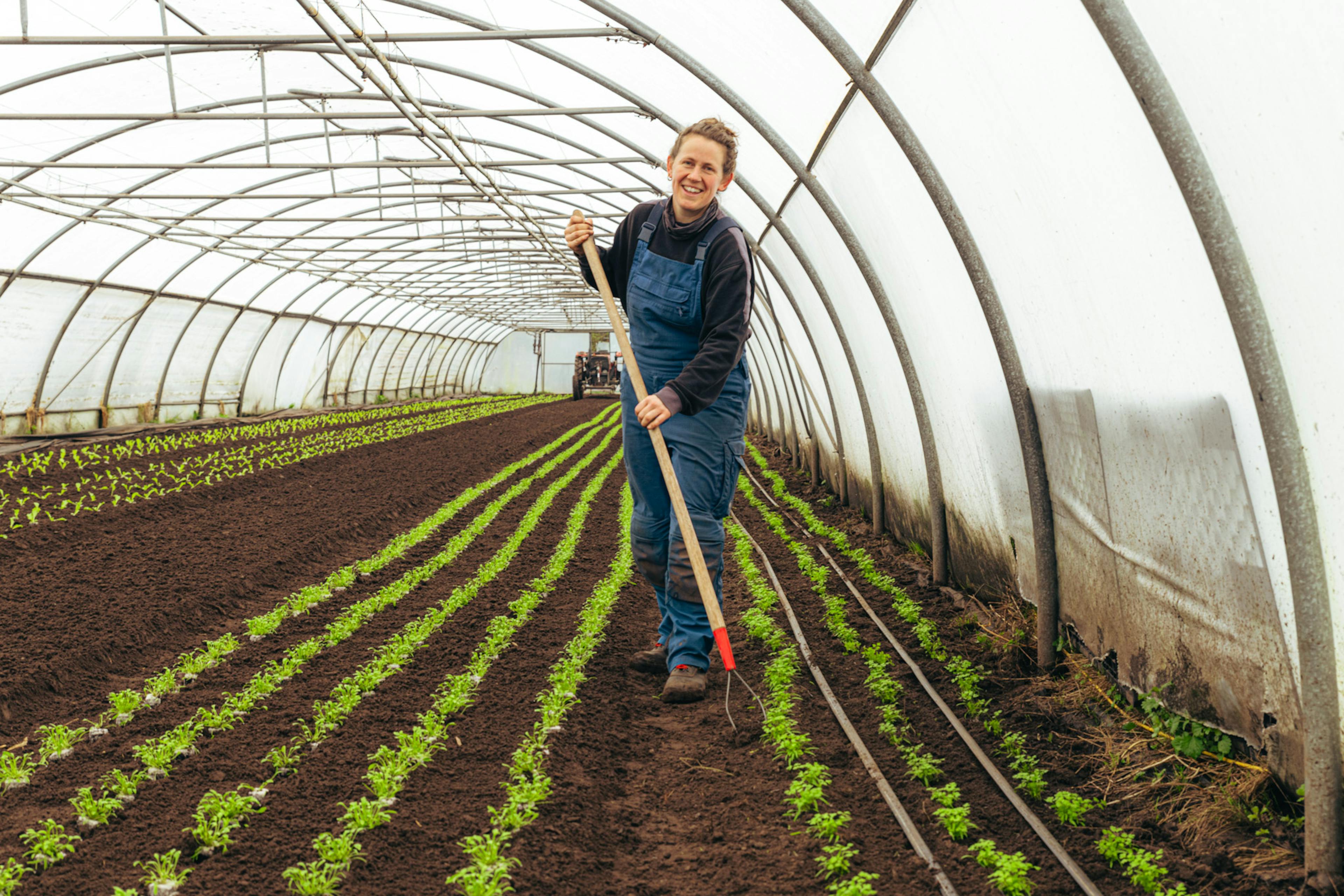 boerin breed glimlachend aan het schoffelen in de serres