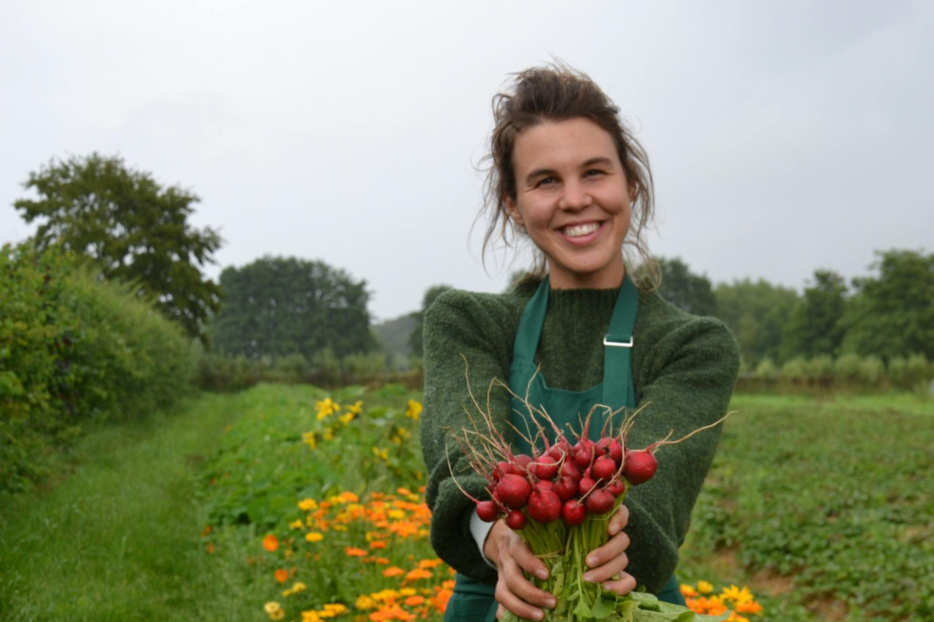 Marie buiten op het veld die een bussel radijzen voor zich uitsteekt