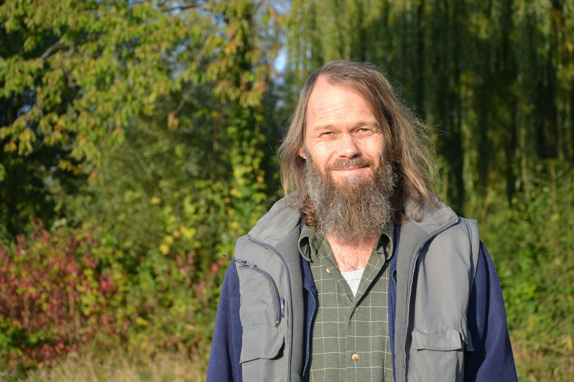 headshot van een glimlachende Dave in de tuin met bomen op de achtergrond