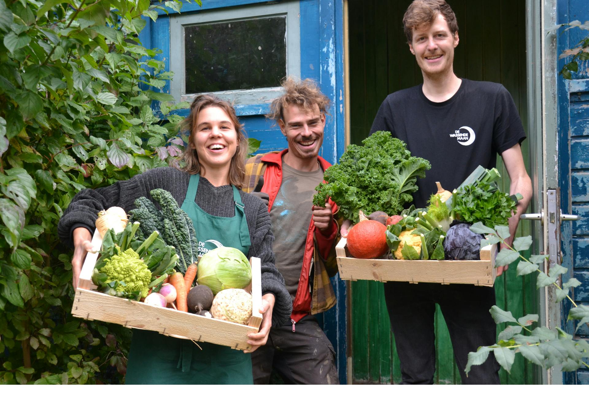 Foto van 3 jonge mensen die lachend poseren met groentepakketten van De Wassende Maan