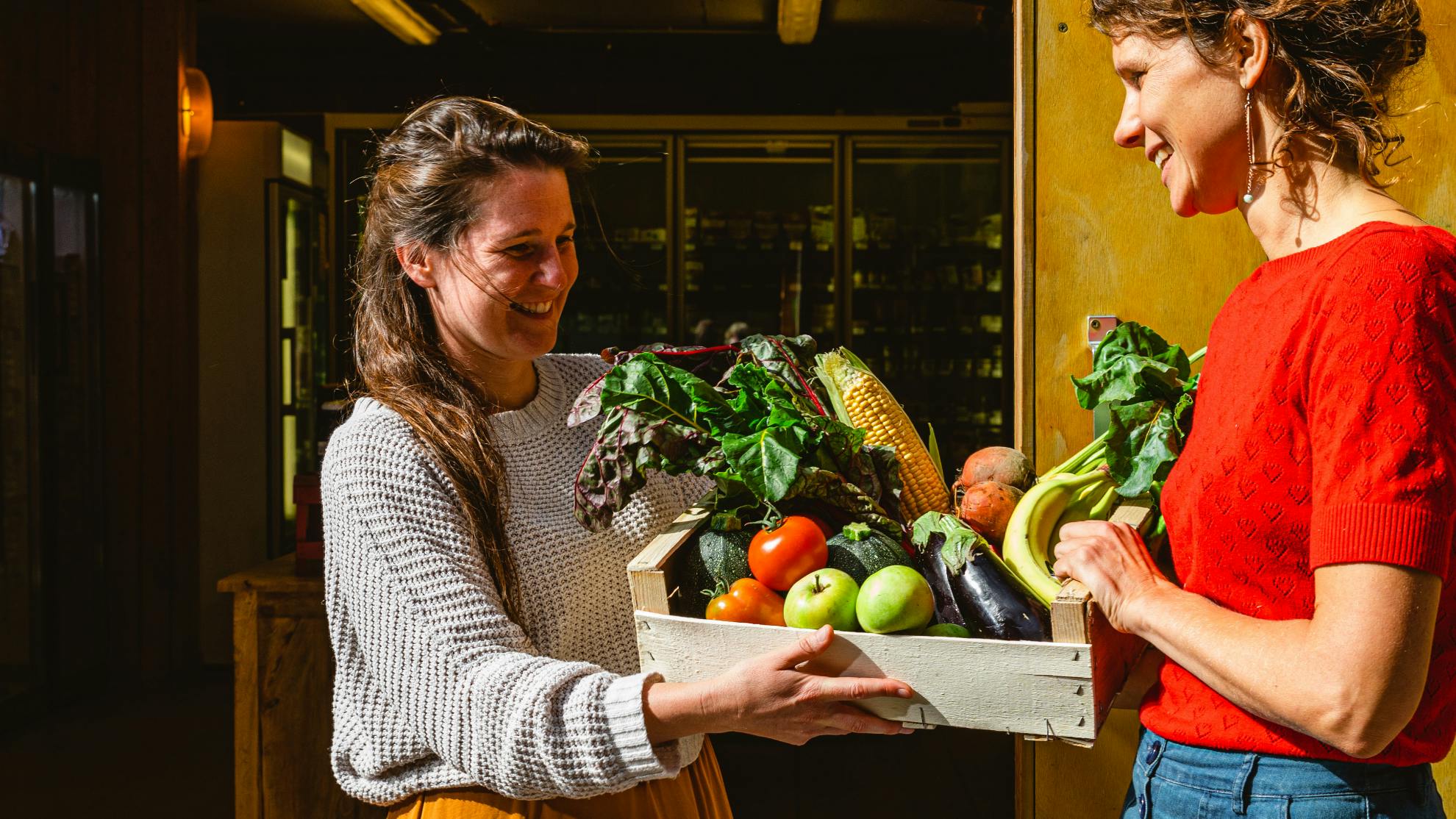 Foto van twee vrouwen die een groentepakket biobox groentepakket van De Wassende Maan vasthouden
