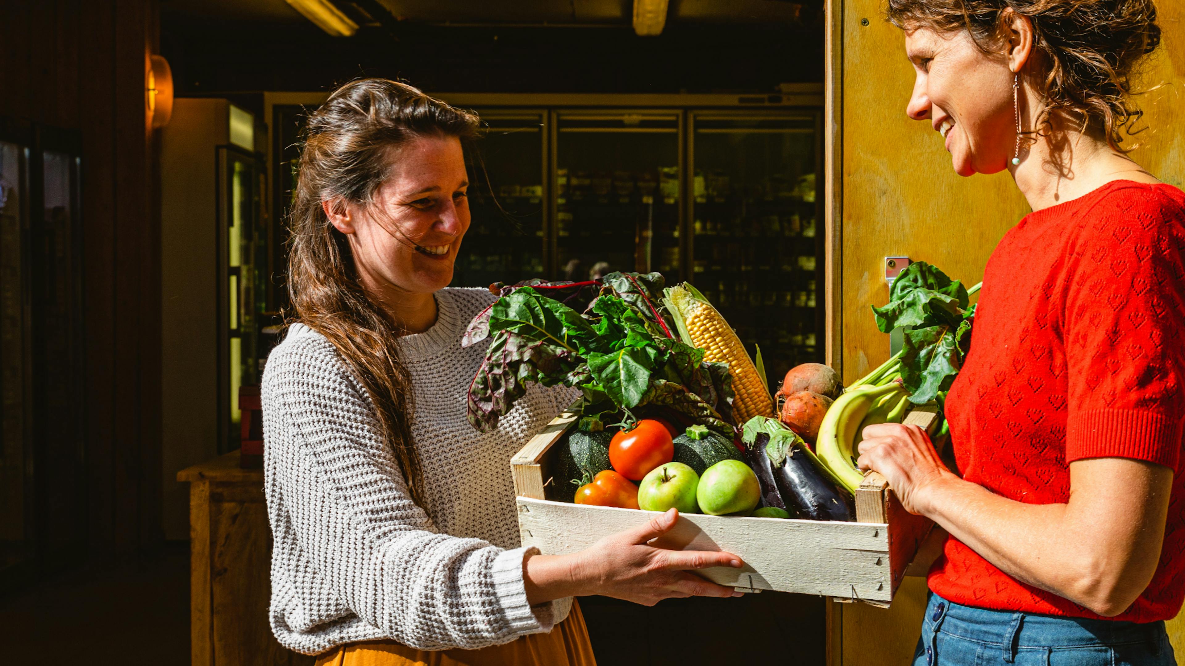 Foto van twee vrouwen die een groentepakket biobox groentepakket van De Wassende Maan vasthouden