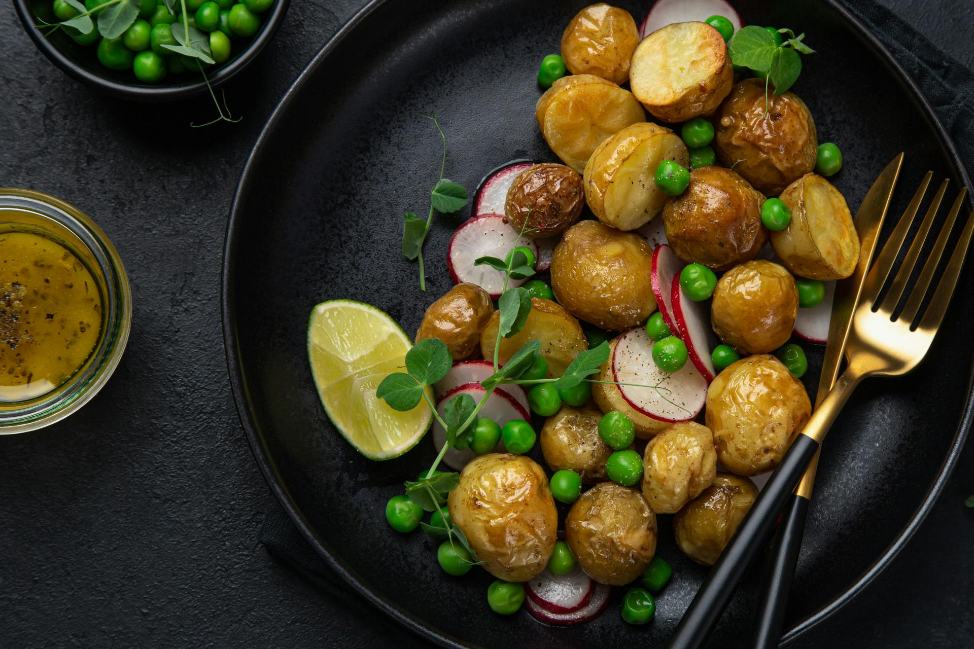 Bord met bestek, gevuld met aardappelsalade, erwtjes en radijs
