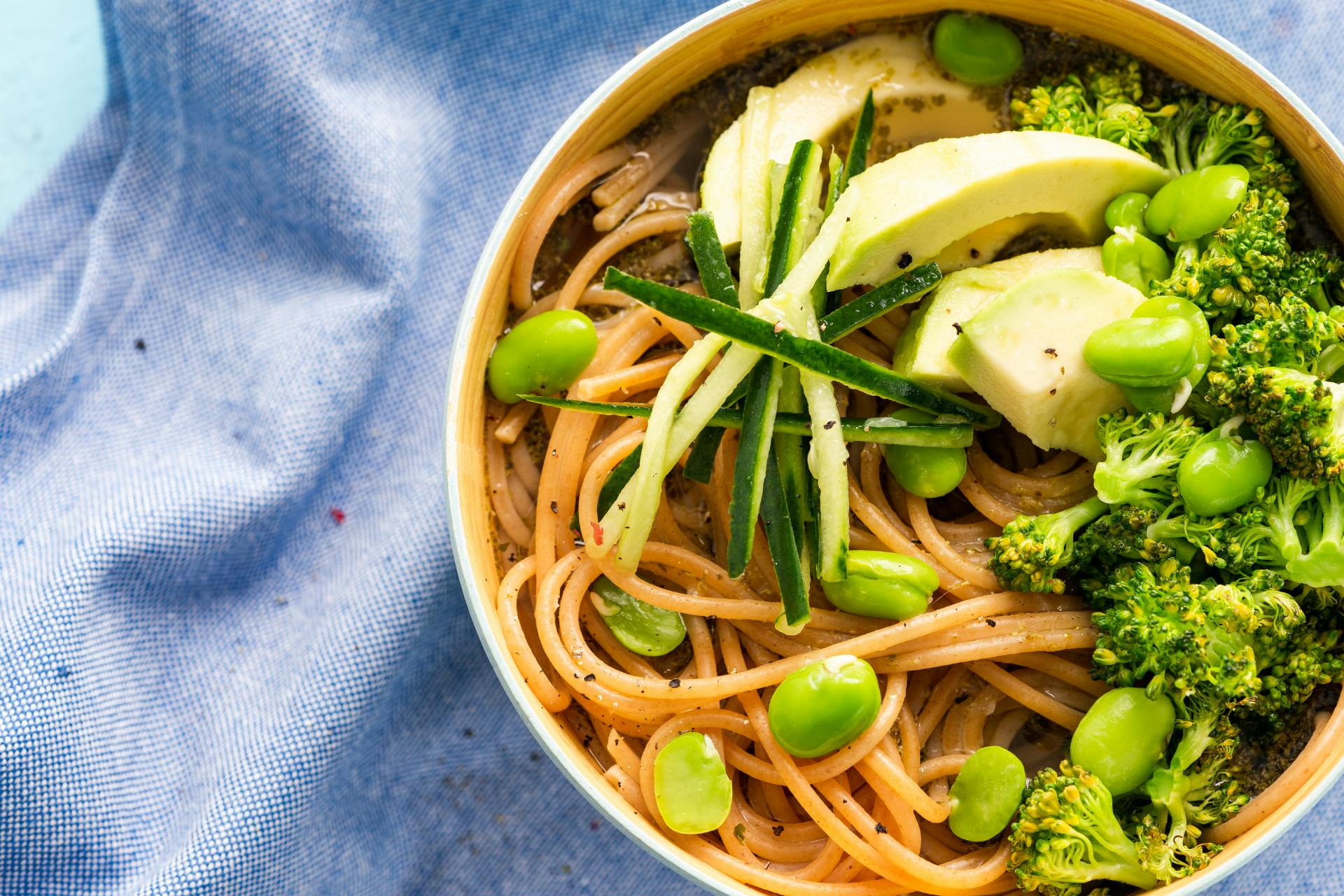 witte kom met noodles, avocado, broccoli, komkommer, courgette en edamameboontjes