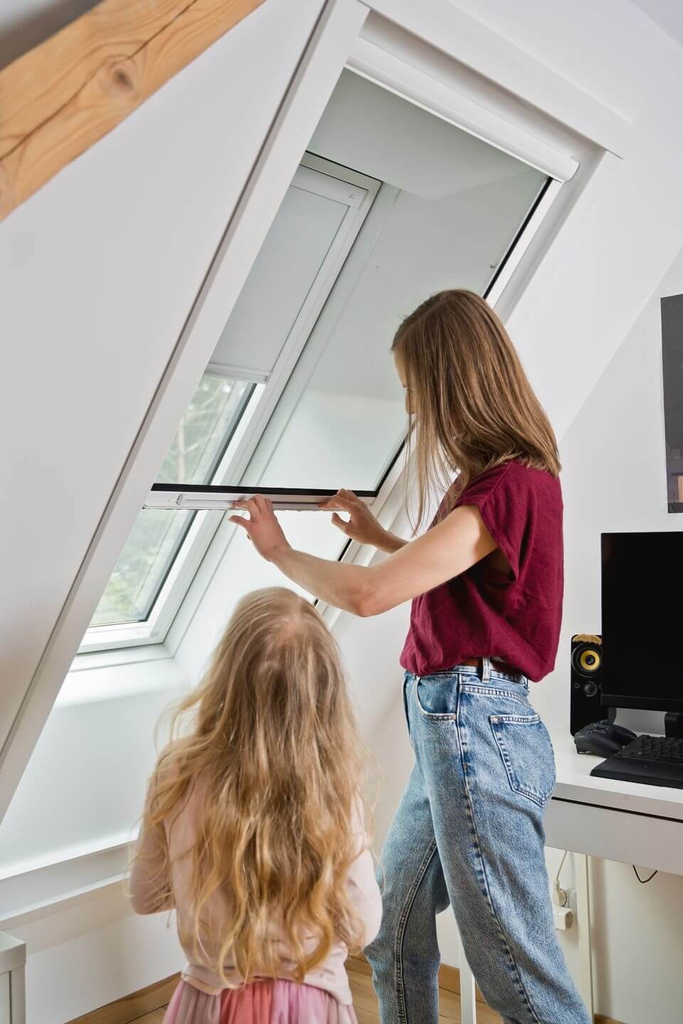 Mädchen schaut ihrer Mutter dabei zu wie sie ein Insektenschutzrollo am Roto Dachfenster schließt