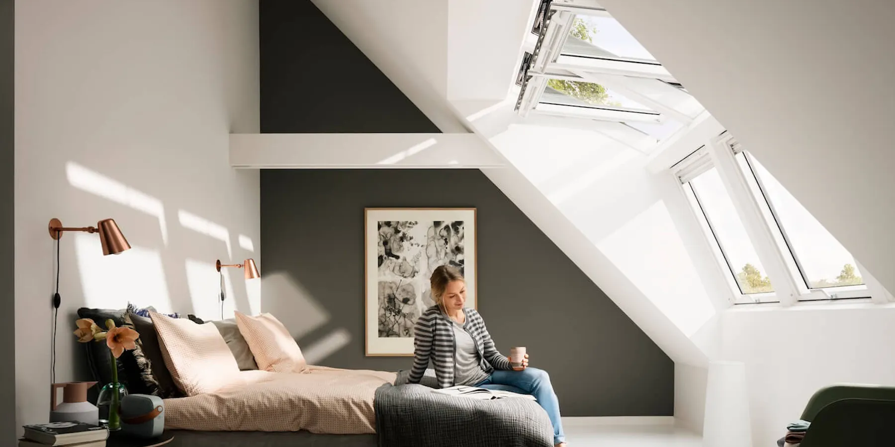 Frau sitzt auf Bett im Schlafzimmer mit hohen Dachfenstern Frau sitzt auf Bett im Schlafzimmer mit hohen Dachfenstern