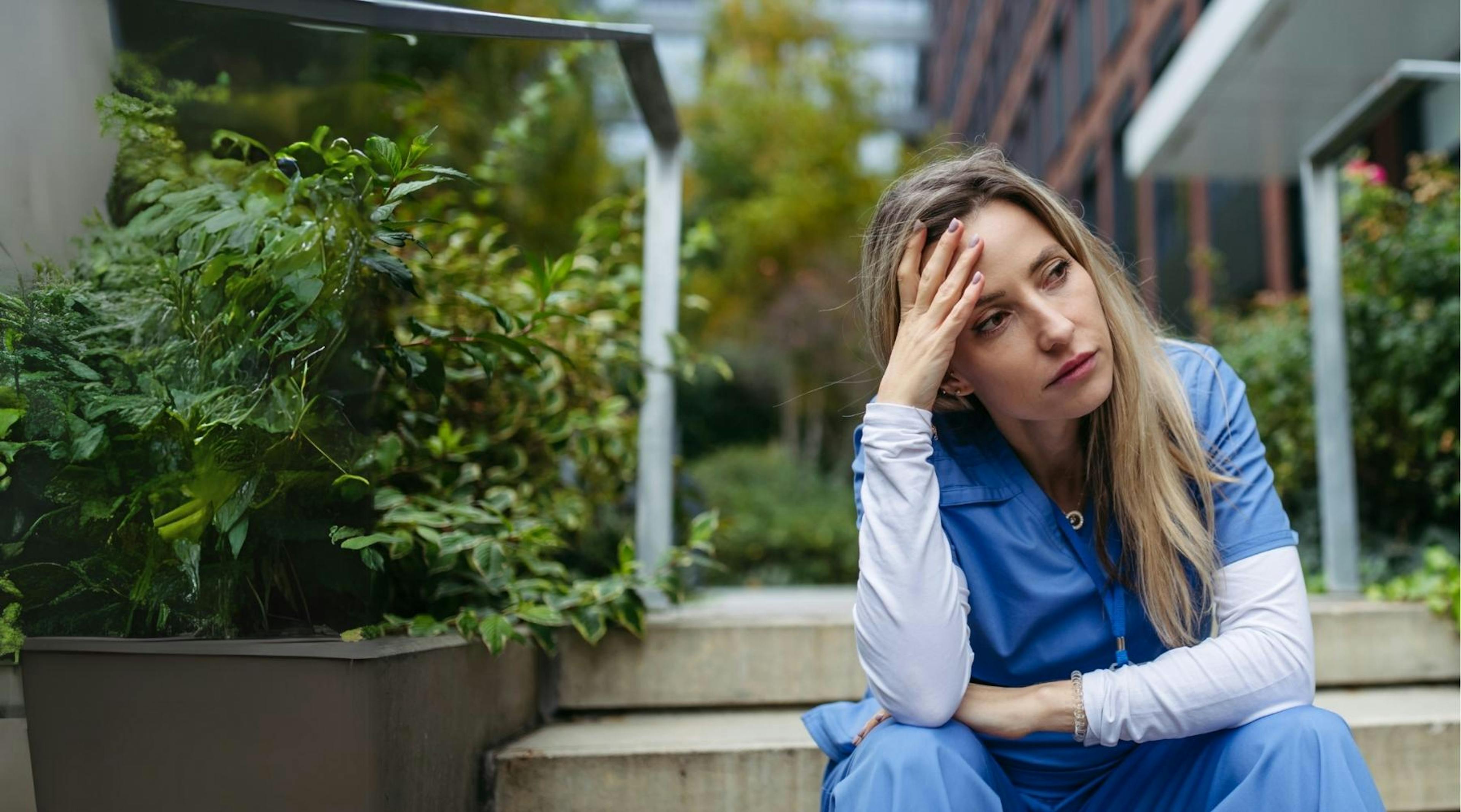Compassion Fatigue: Eine Pflegekraft sitzt erschöpft vor einem Krankenhaus