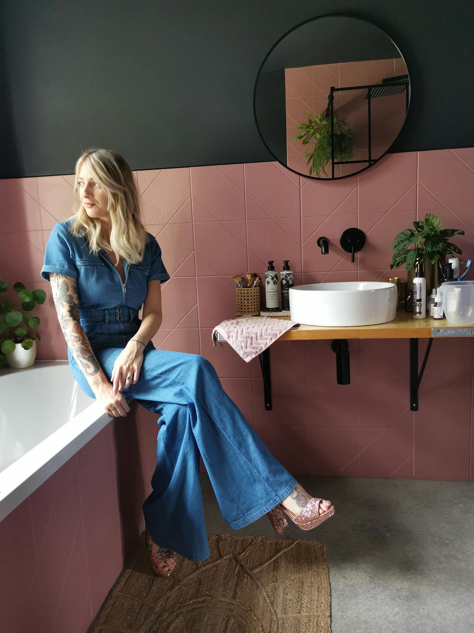 Blonde woman in a bathroom painted in black with pink tiles