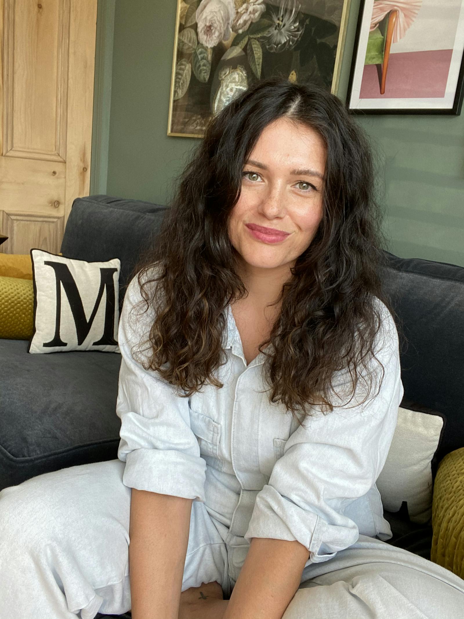 Woman with wavy hair sitting on a navy blue sofa in front of a sage green wall