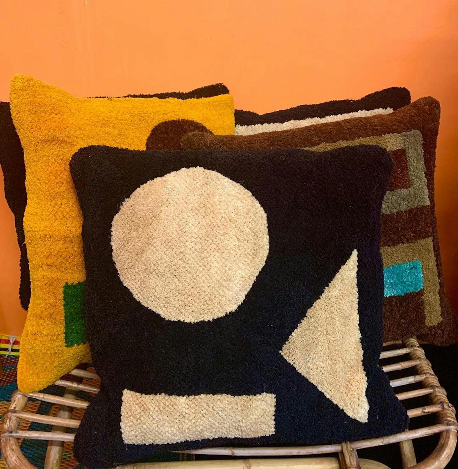 A stack of pillows in a kuba / raffia material against a bright orange wall