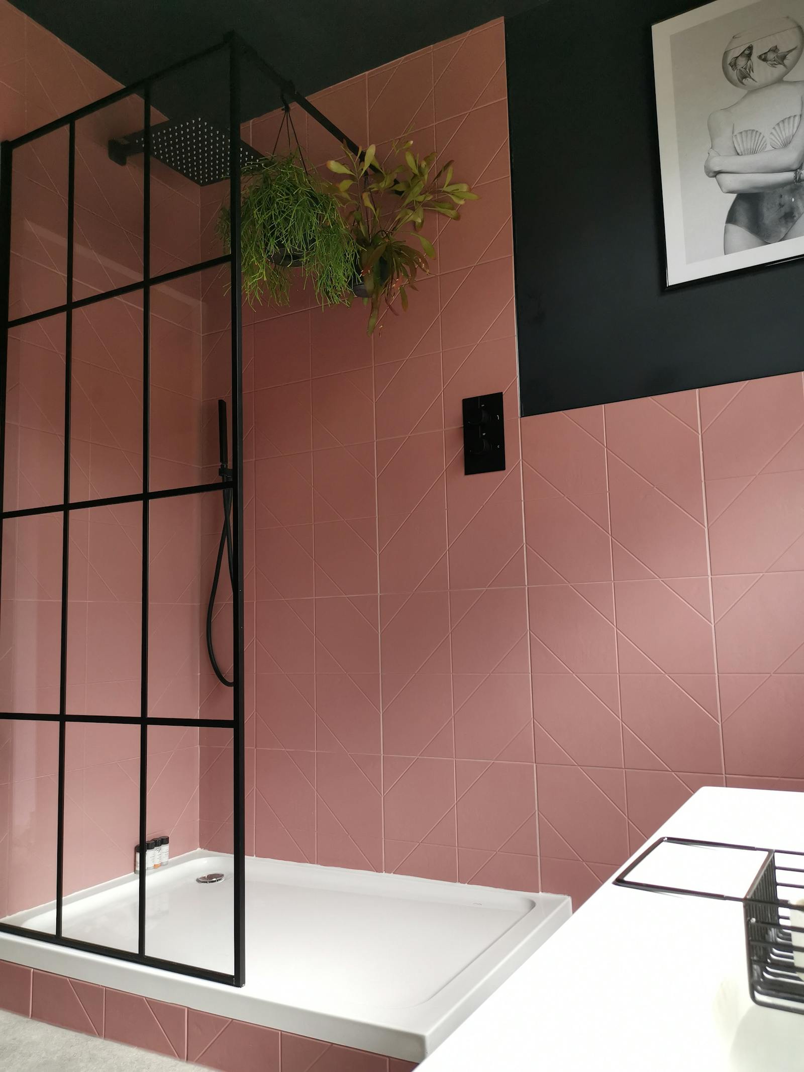Shower area in a bathroom painted in black with pink tiles