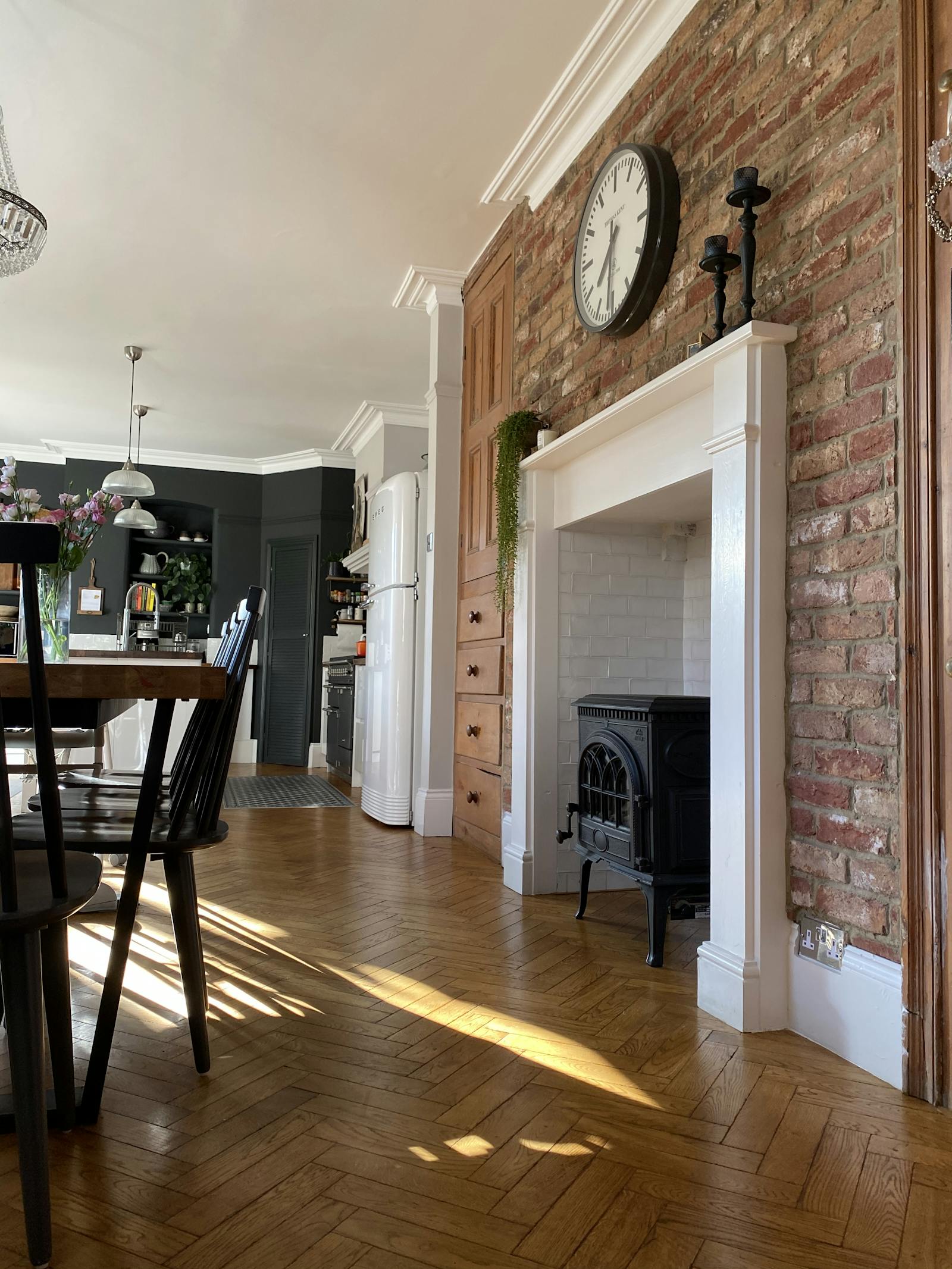Dining room with a brick wall and a fireplace, overlooking a kitchen wall painted in black