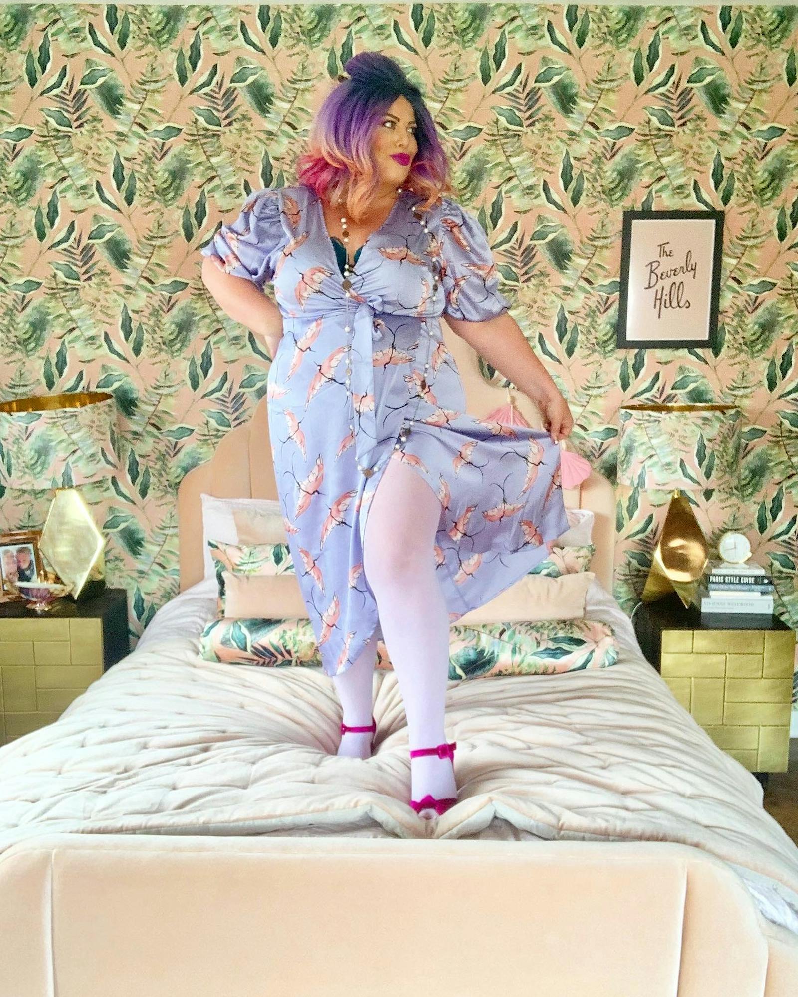 woman with purple hair and purple dress posing in front of a leaf-patterned wallpaper