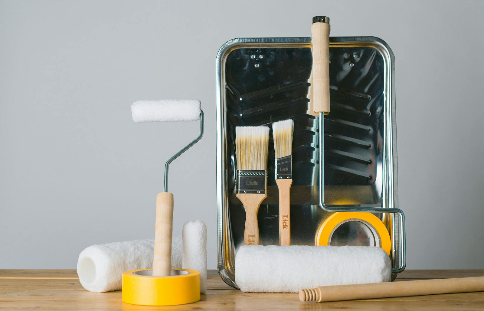 A collection of Lick painting and decorating tools including yellow tape, brushes, rollers and a tray.