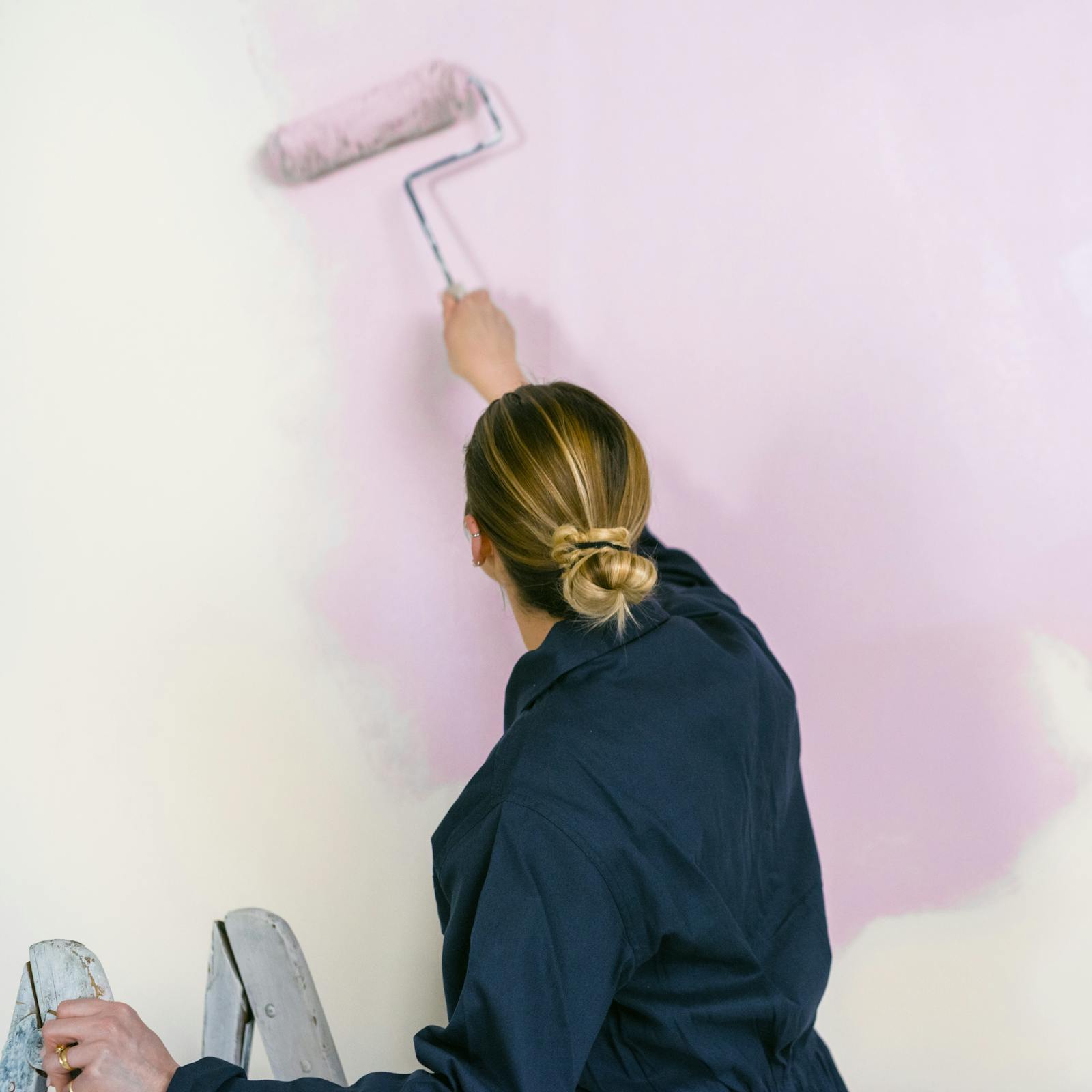 Blonde woman painting a pink paint on wall with a roller brush
