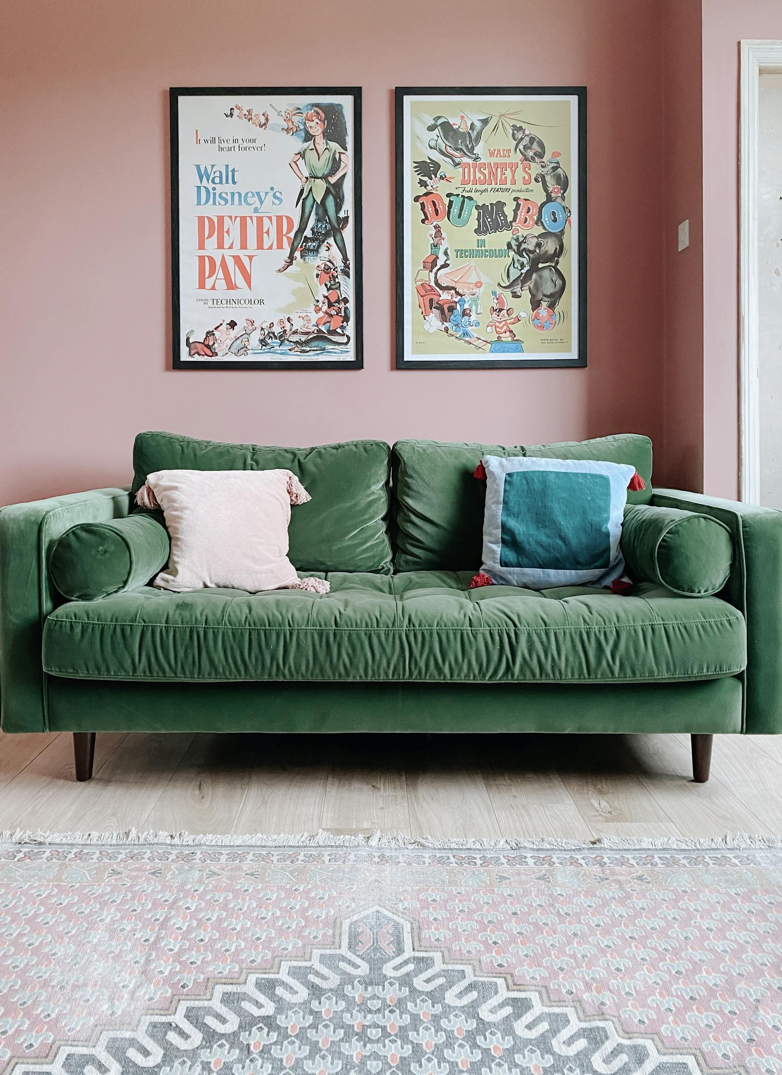 Green velvet three-seater sofa on wooden floor against a bubblegum pink wall with Disney posters