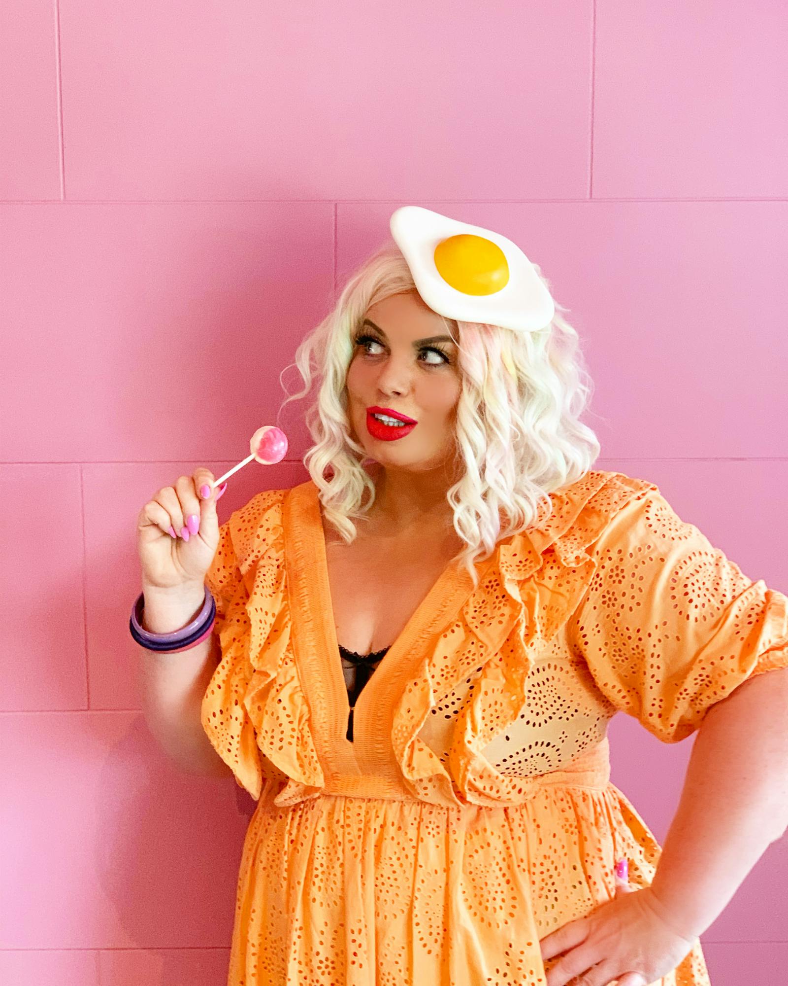 woman in an orange dress posing in front of a bubblegum pink tiled wall