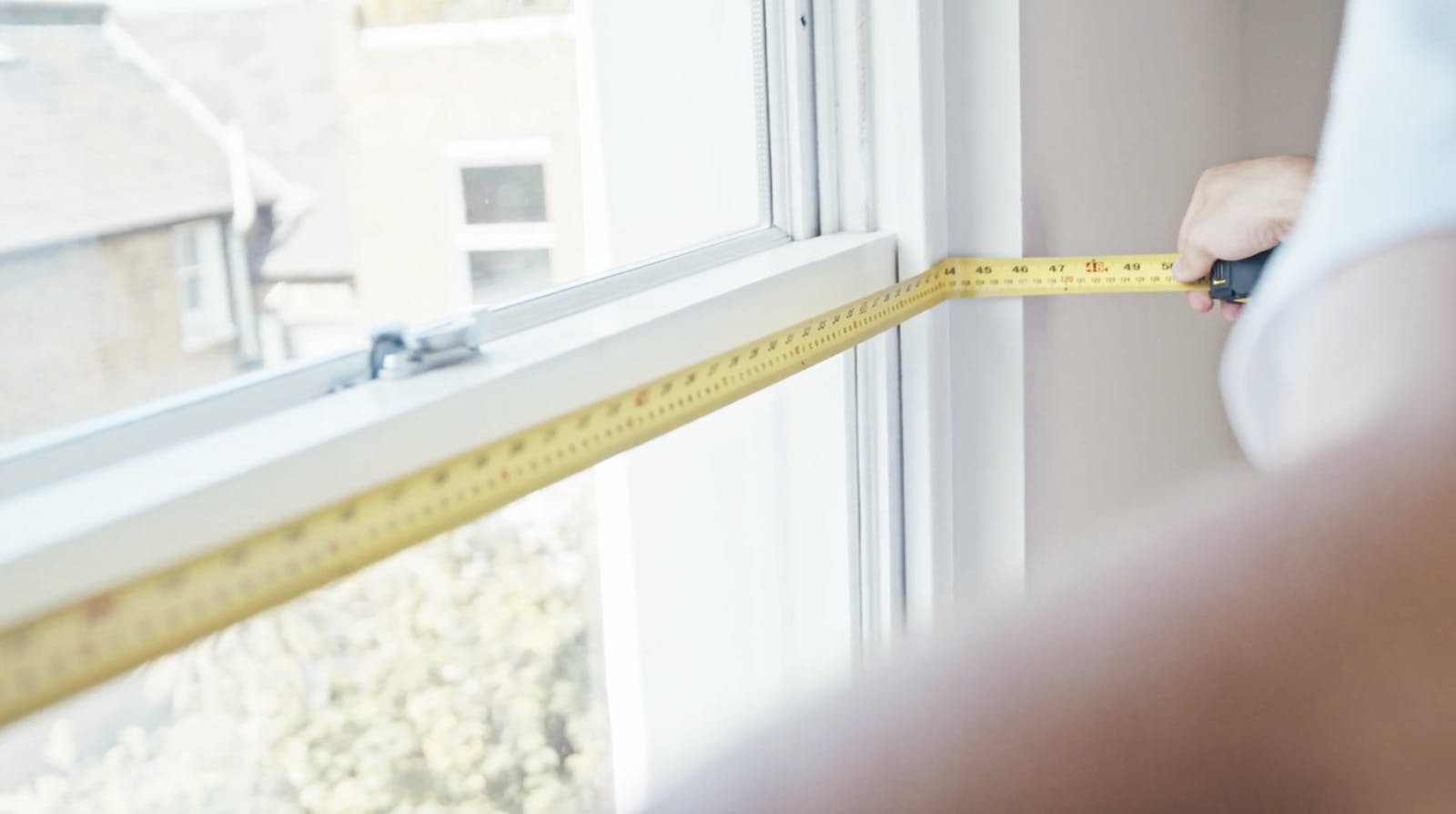 Man holding metal tape measure against window recess