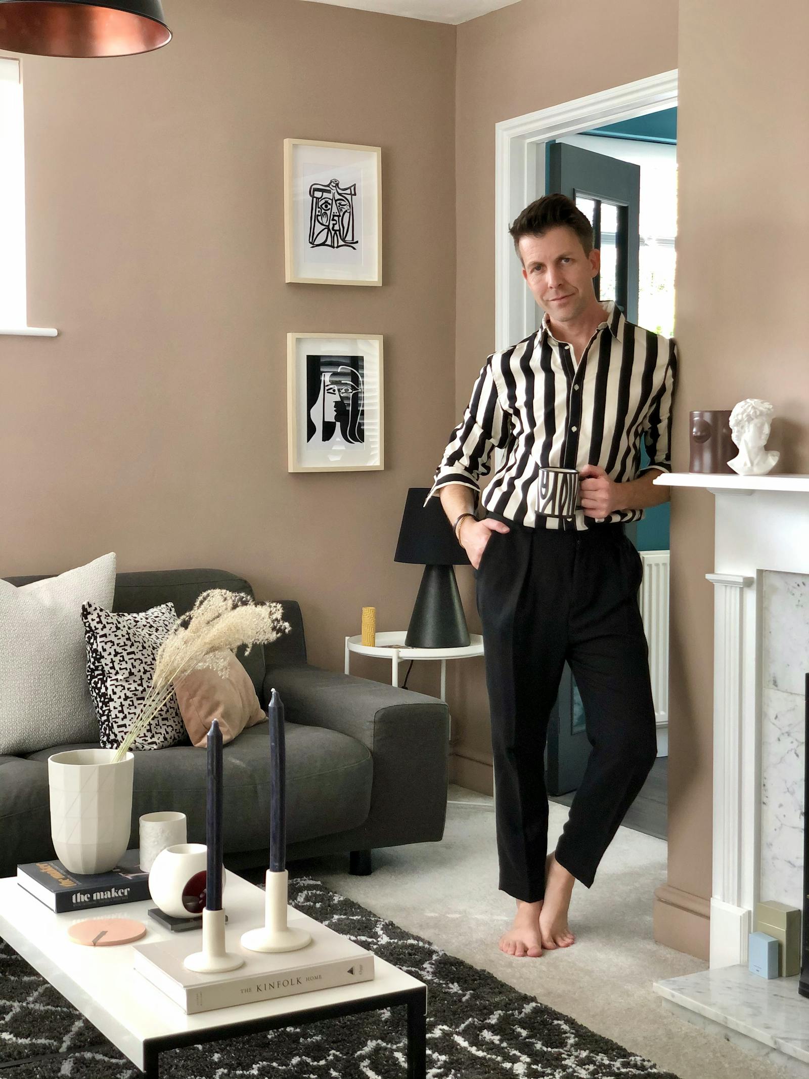 Man standing in neutral beige painted living room with grey velvet sofa and black and white soft furnishings