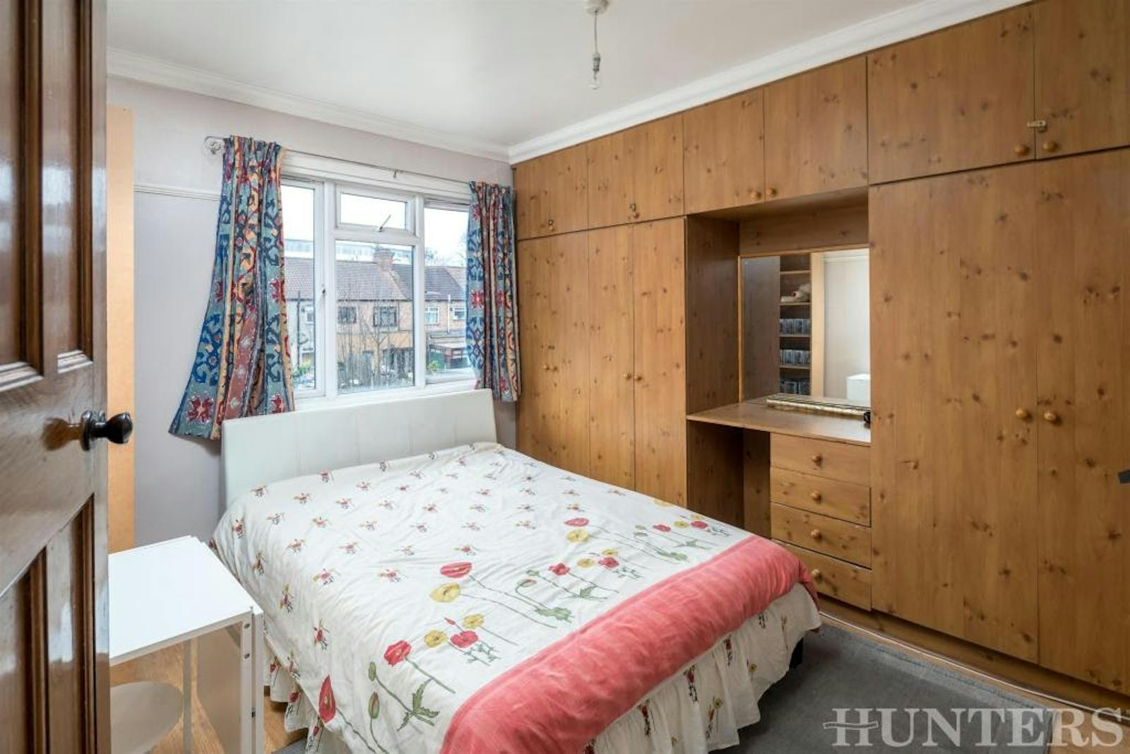 Photo of dated bedroom with wooden cupboards and floral bed linen