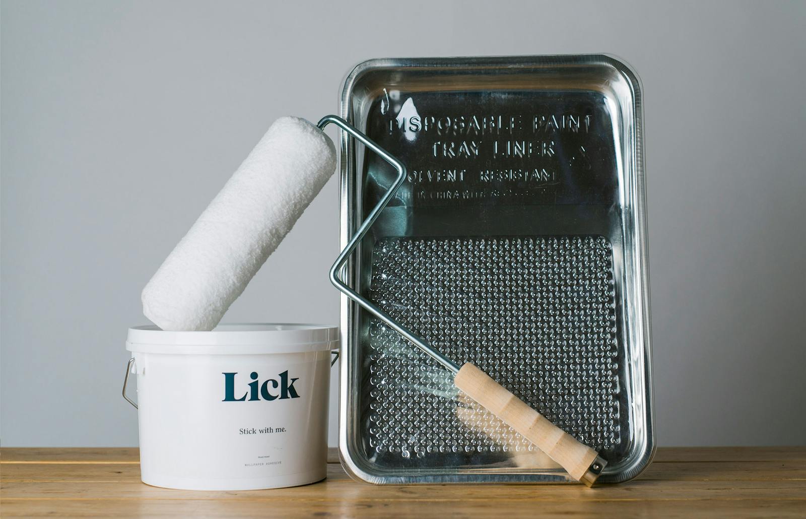 An essential collection of Lick wallpapering tools including a roller, adhesive, metal tray and plastic cover.