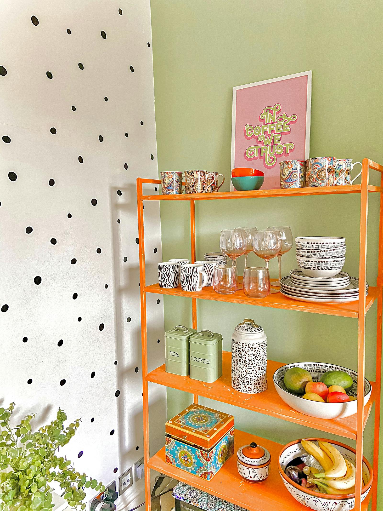 Brightly coloured kitchen with polkadot wallpaper and an orange shelf for plates and glasses