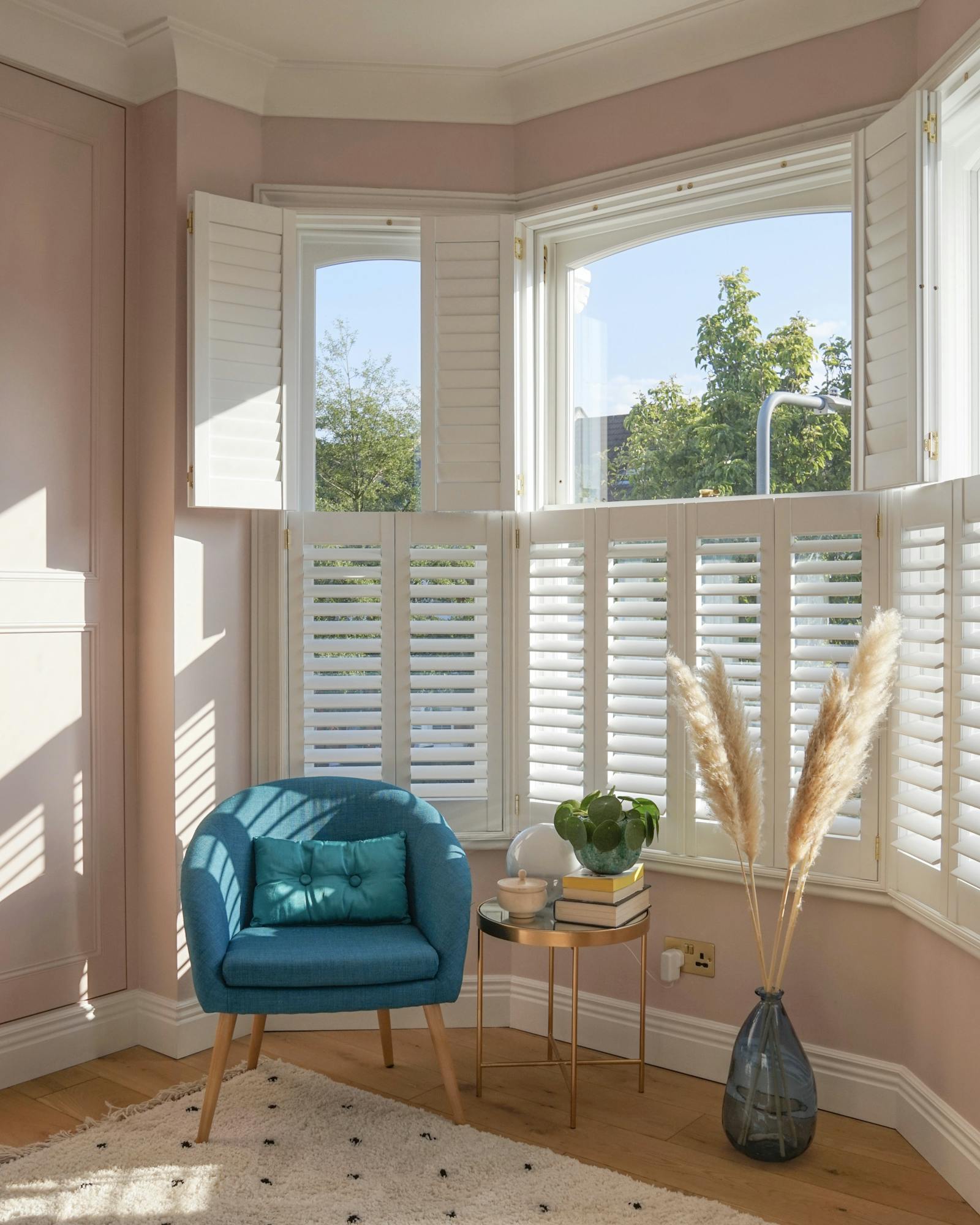 Corner of a bedroom with a lot of natural light coming from the windows and a blue armchair with a cushion on it