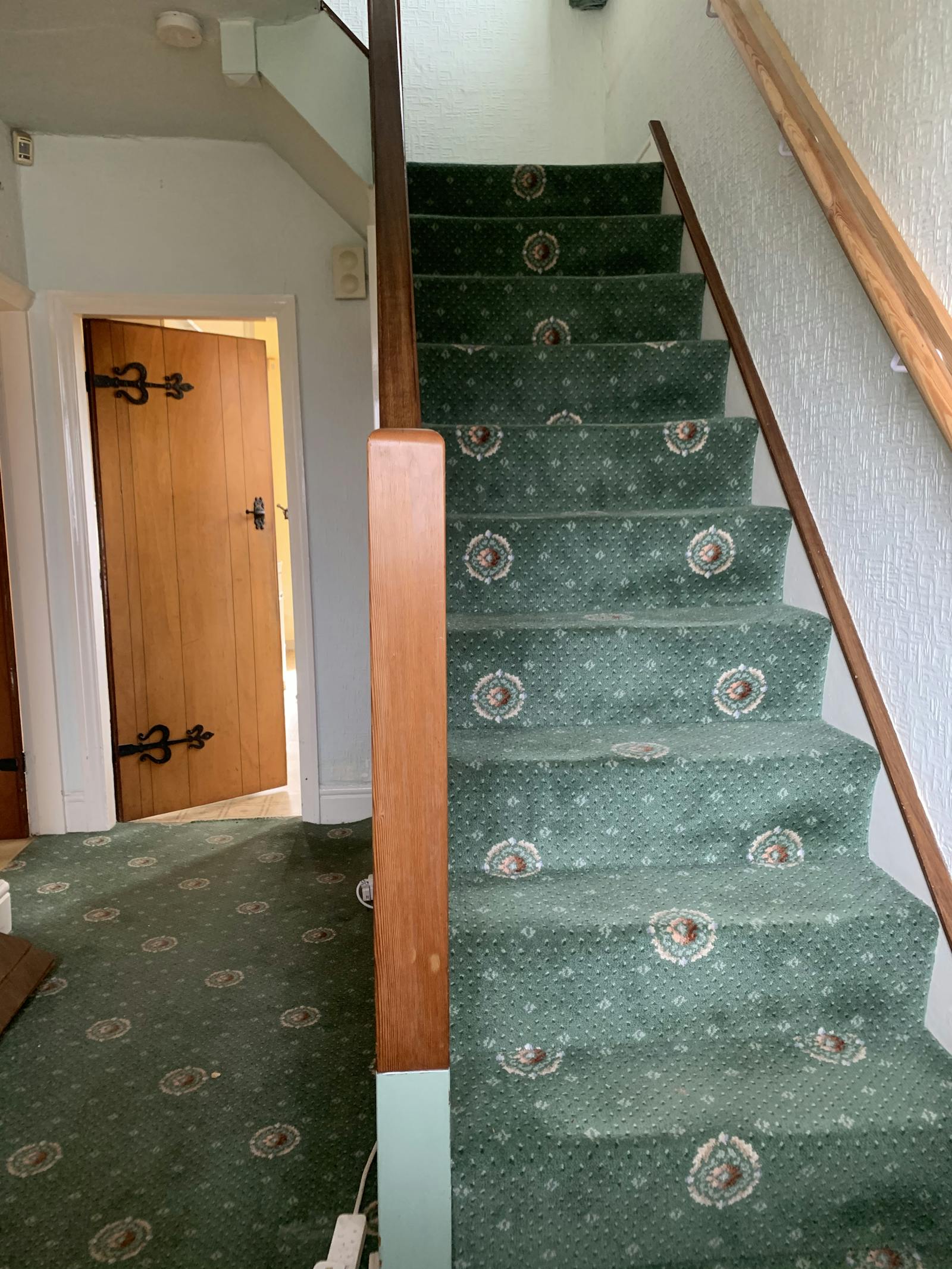 Image of hallway with dated green carpet running up stairs