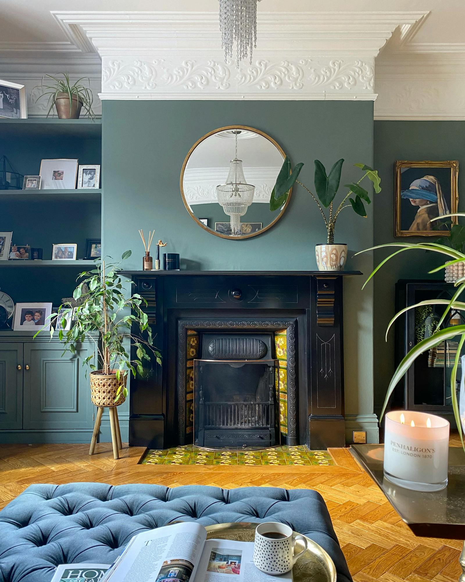 Living room painted in sage green with natural wood floor, navy blue sofa and plants