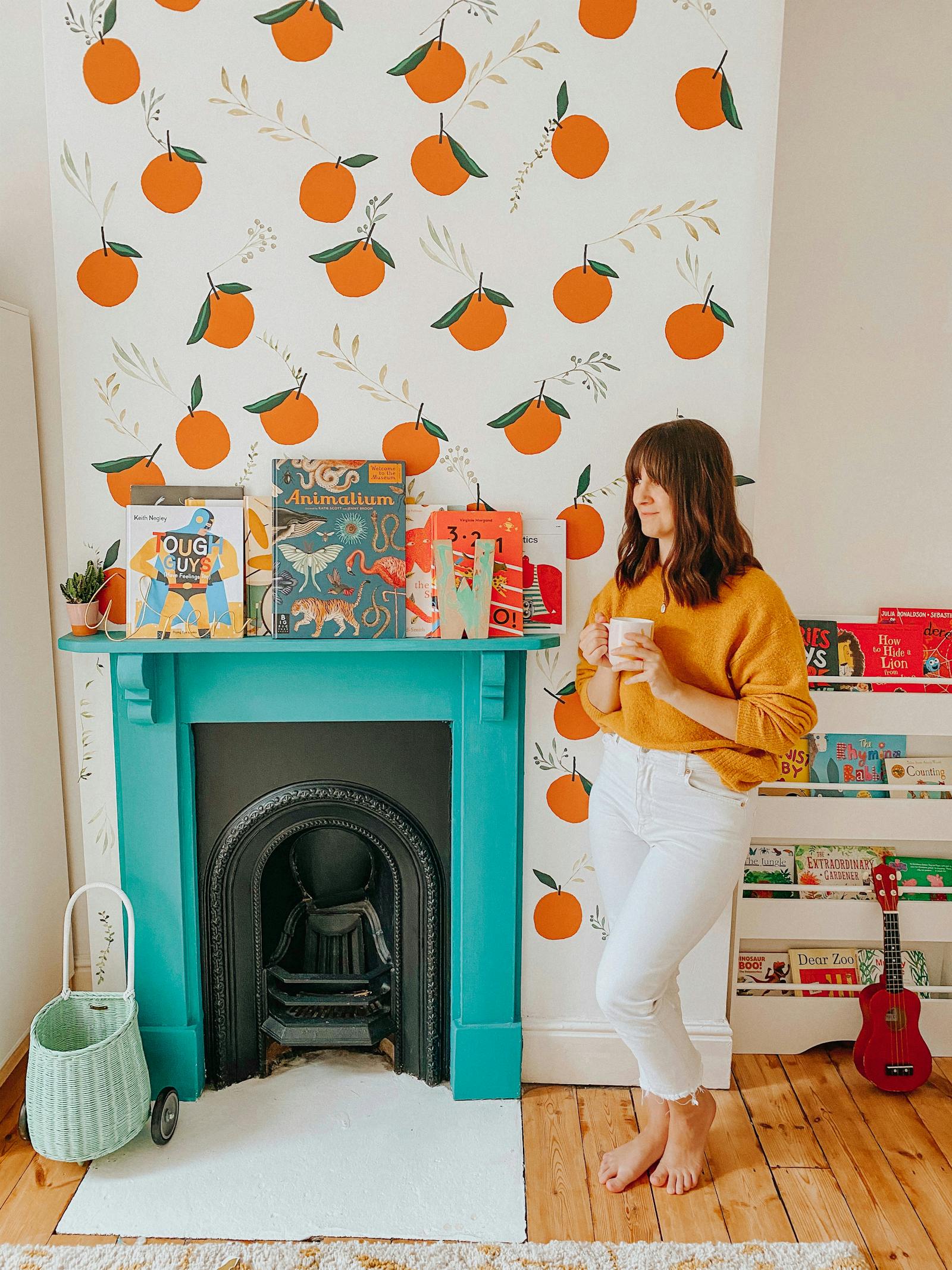 Brunette woman standing in front of turquoise fireplace with orange illustrated wallpaper