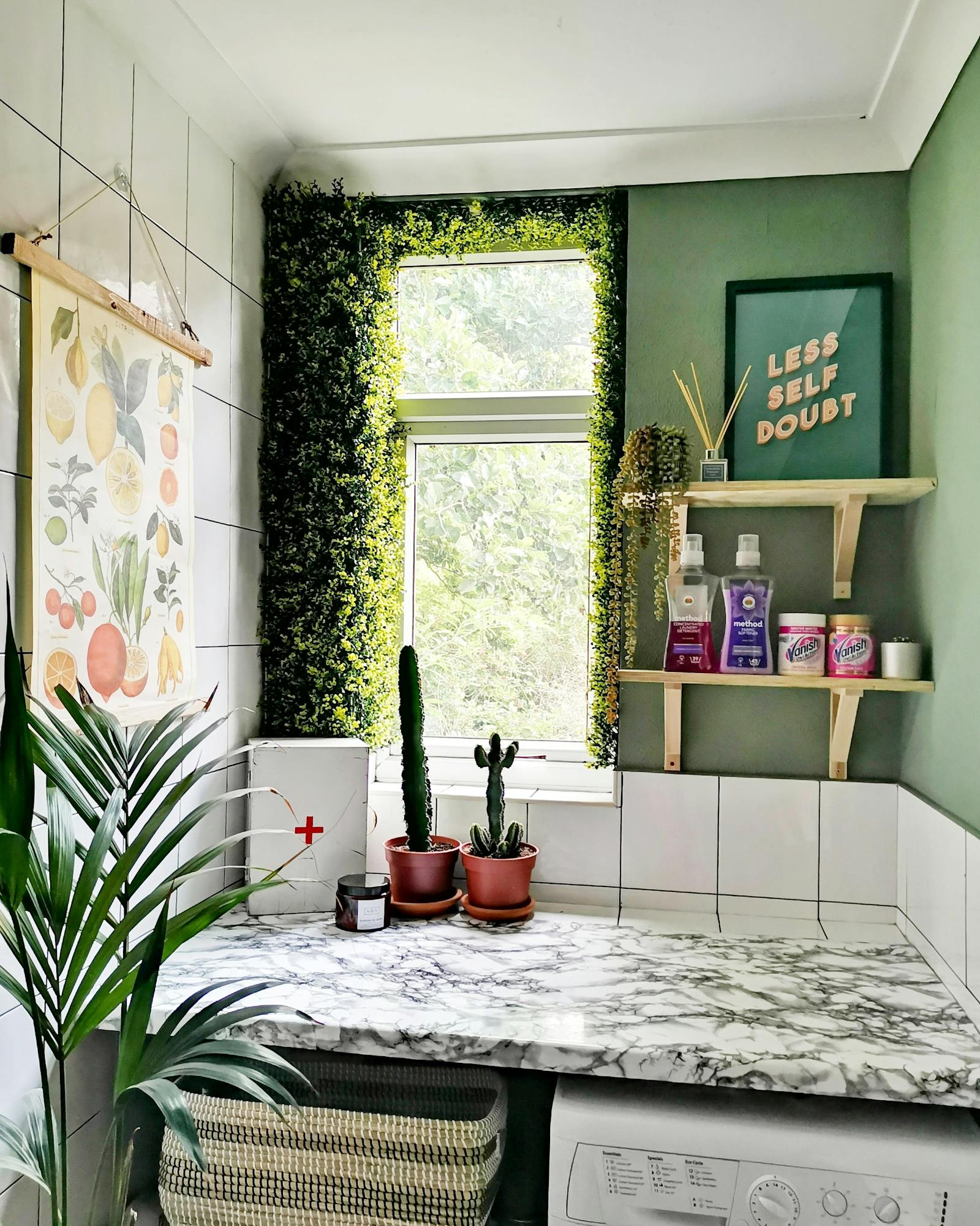 Laundry room painted in light green with a marble top and faux greenery window feature