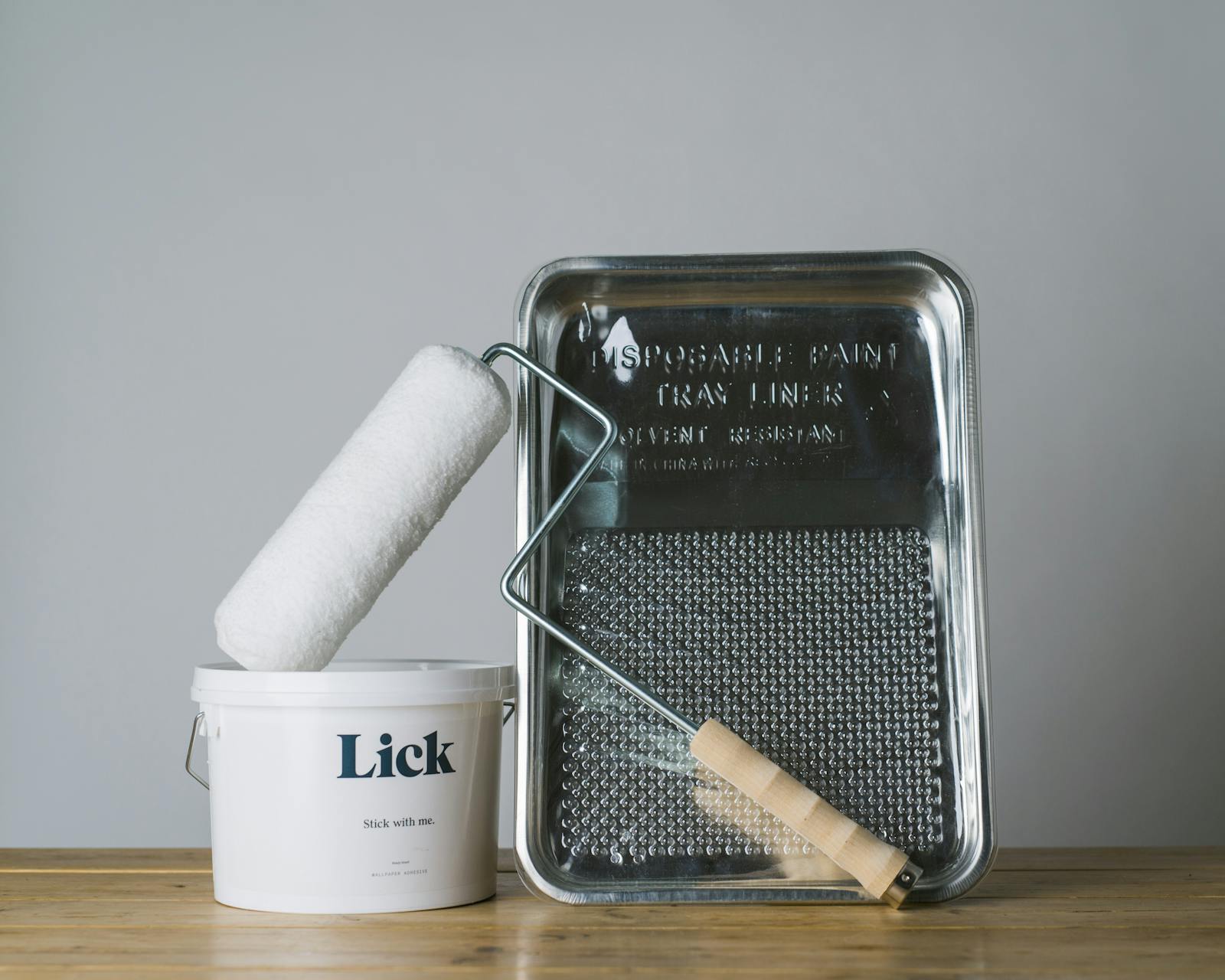 An essential collection of Lick wallpapering tools including a roller, adhesive, metal tray and plastic cover.