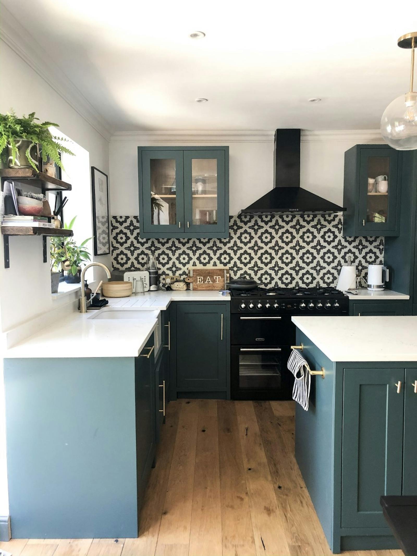 Kitchen with cabinets painted in teal and patterned black and white tiles behind the stove