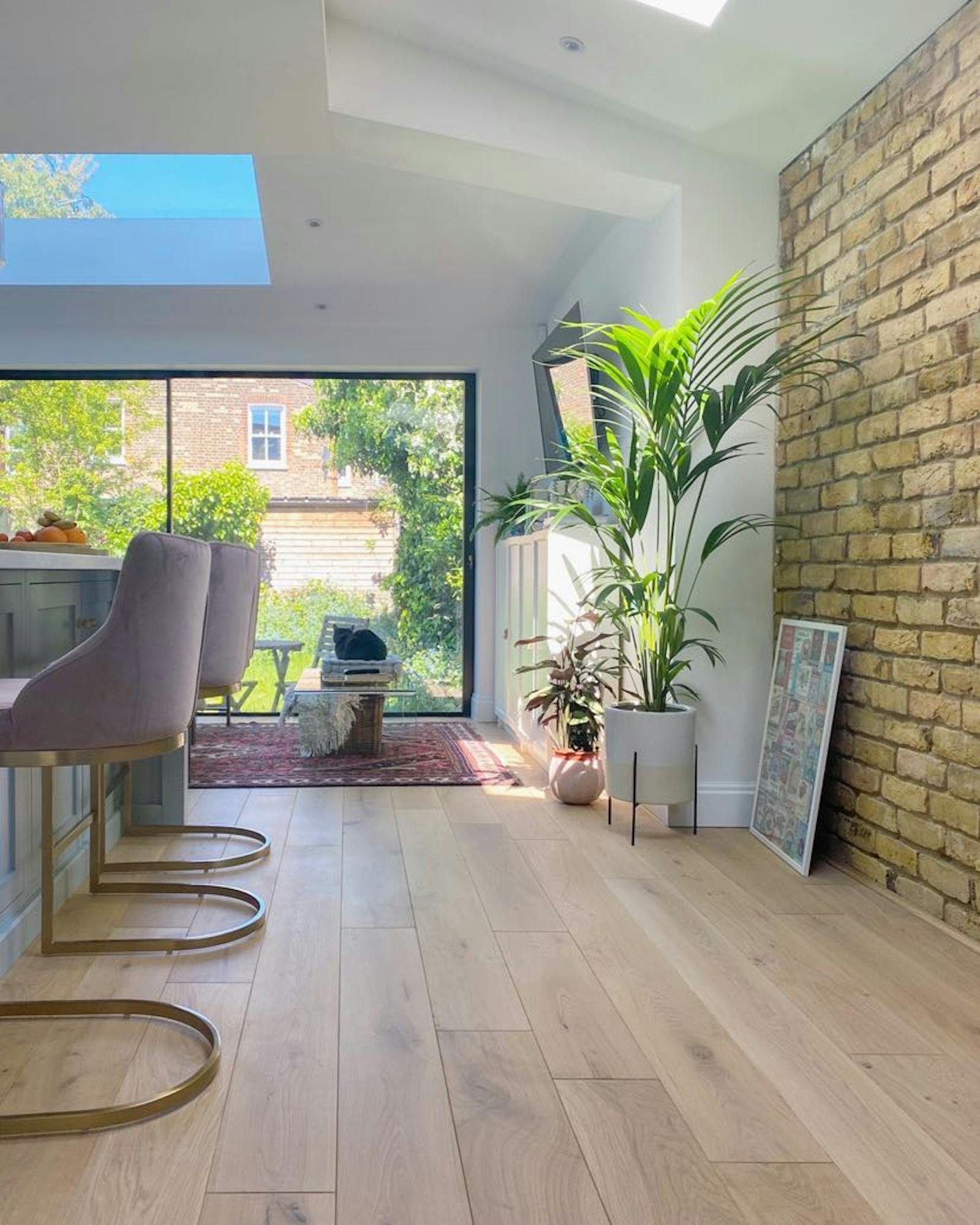 One corner of a dining room with a brick wall and a big plant in front of it