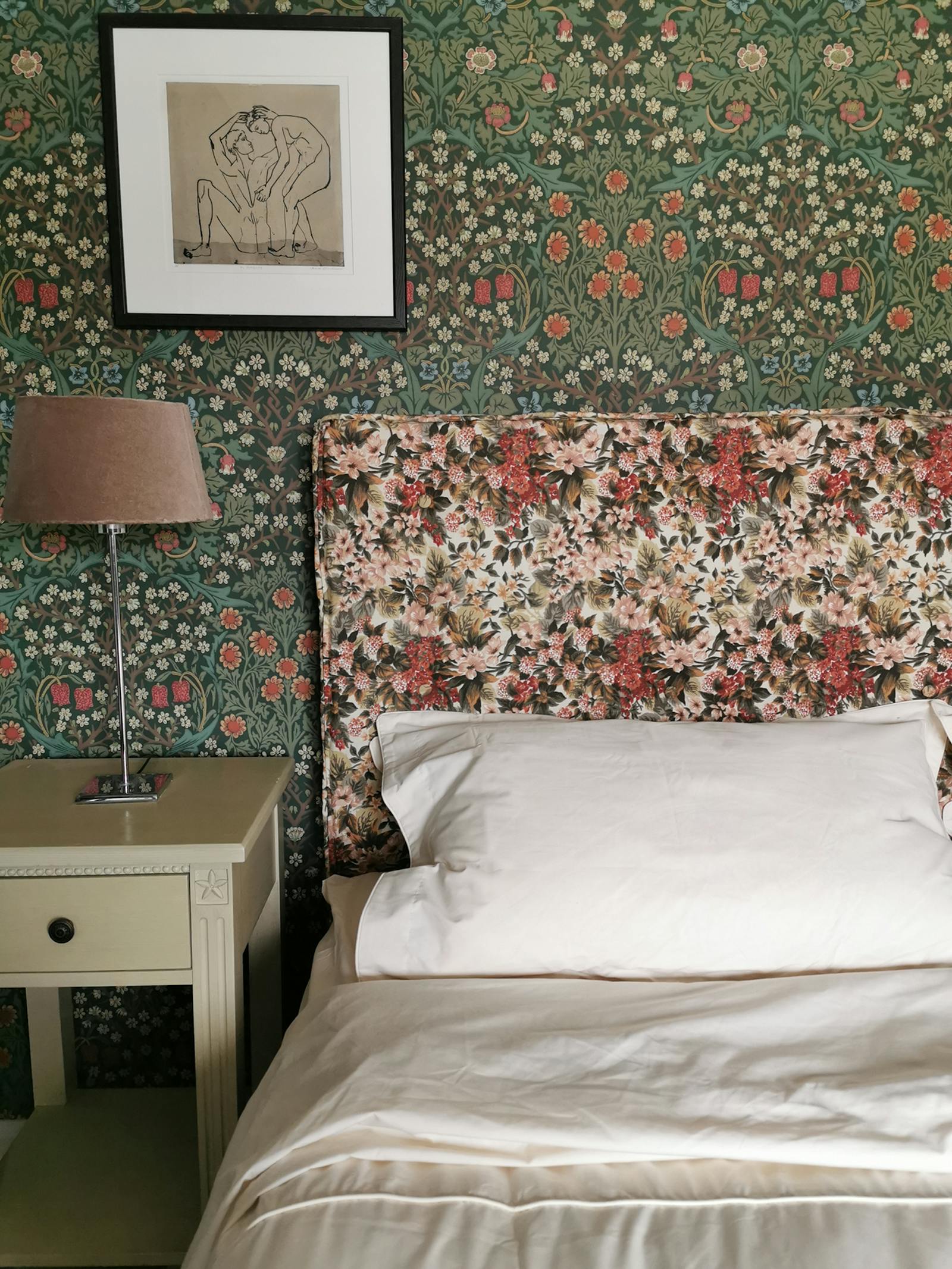 bedroom with a floral headboard and a floral patterned wallpaper with artwork