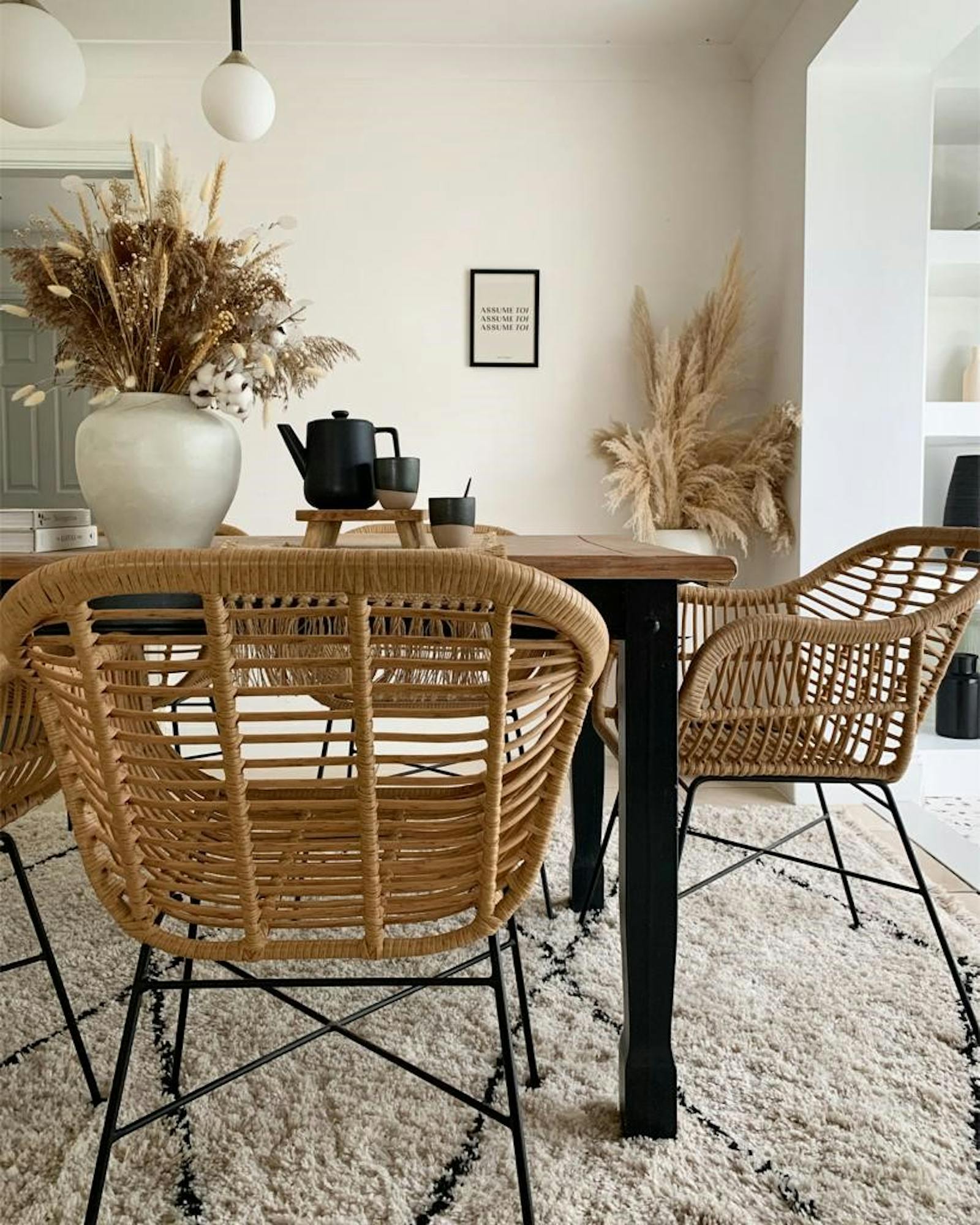 Wooden dining table with rattan chairs and dried foliage in vases